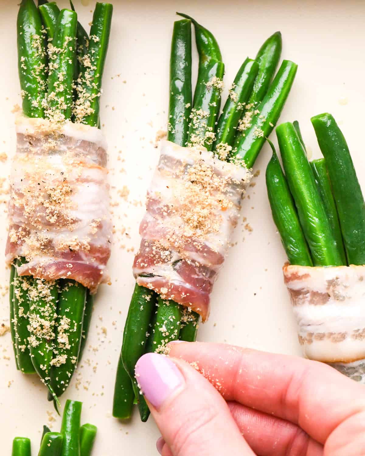 brown sugar mixture being sprinkled over 3 bunches of Bacon Wrapped Green Beans