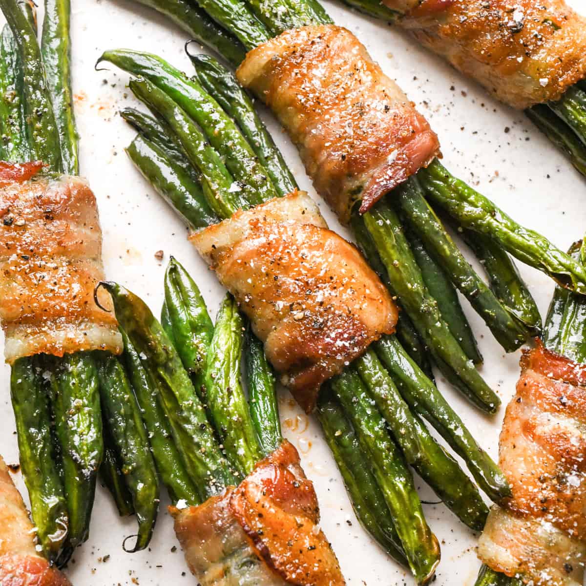 6 bundles of bacon wrapped green beans sprinkled with salt and black pepper on a white plate
