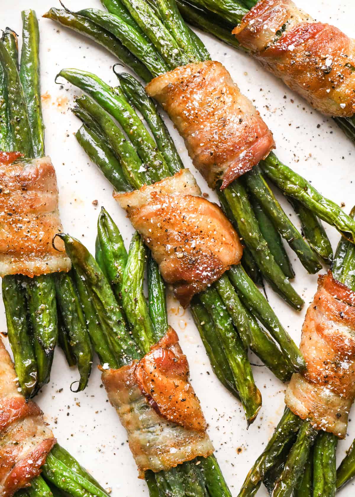 6 bundles of bacon wrapped green beans sprinkled with salt and black pepper on a white plate