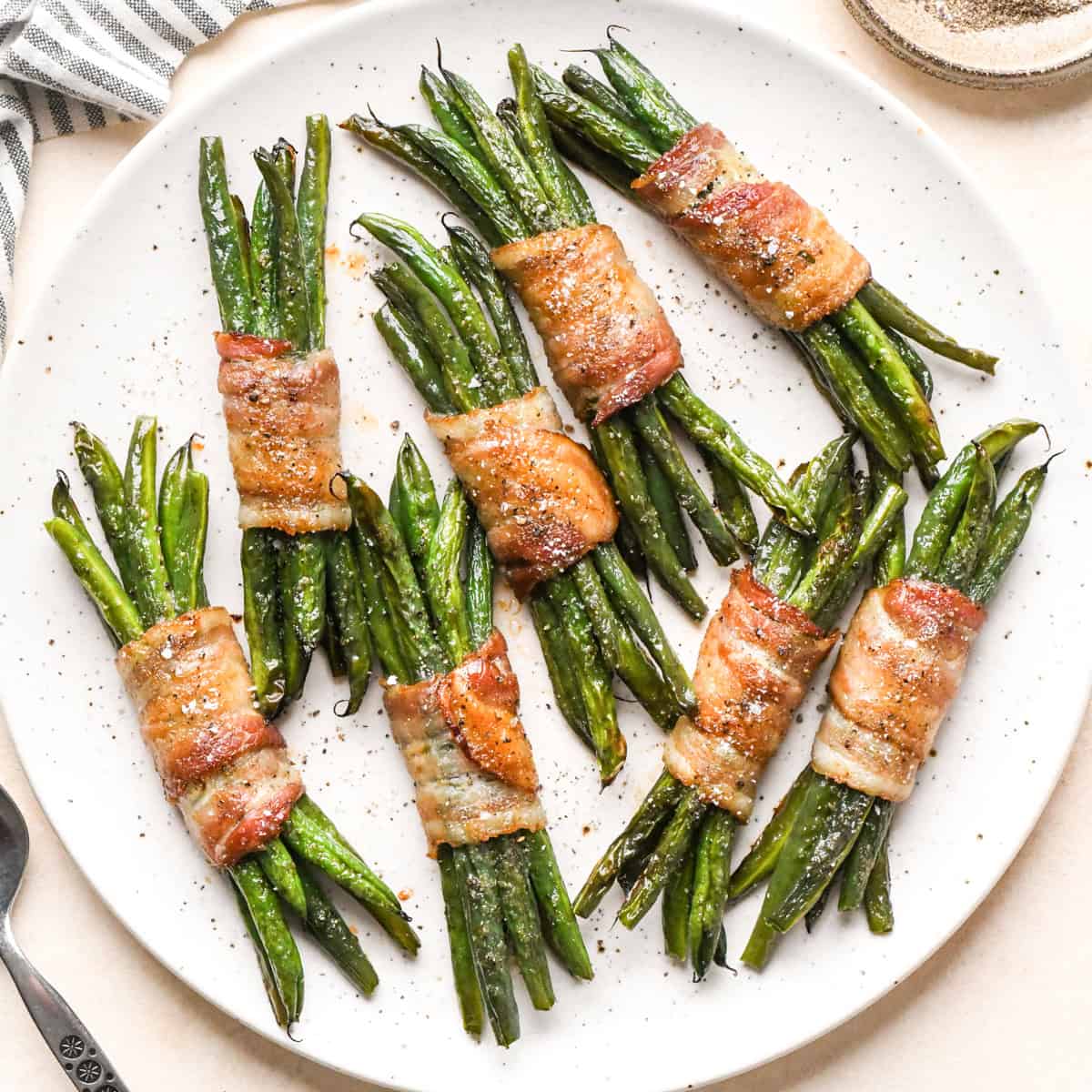 8 bundles of bacon wrapped green beans sprinkled with salt and black pepper on a white plate