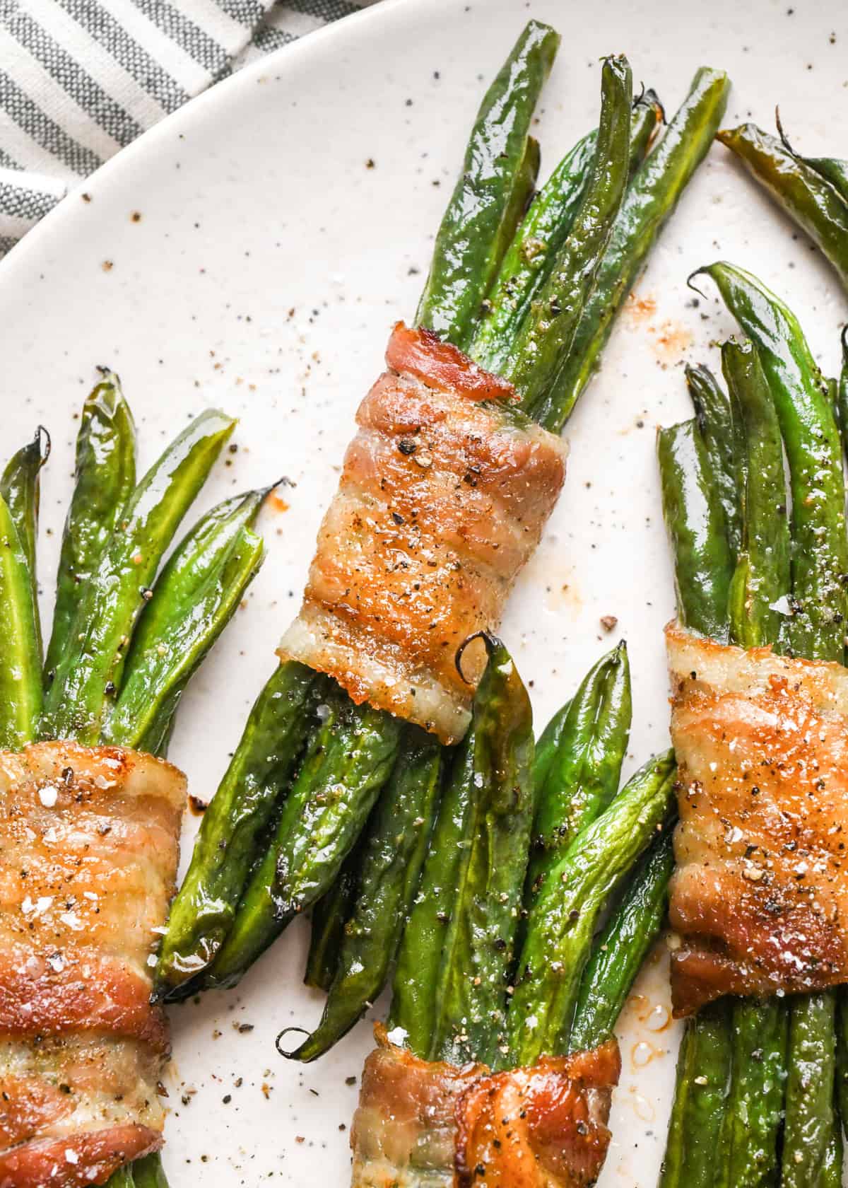 4 bundles of bacon wrapped green beans sprinkled with salt and black pepper on a white plate
