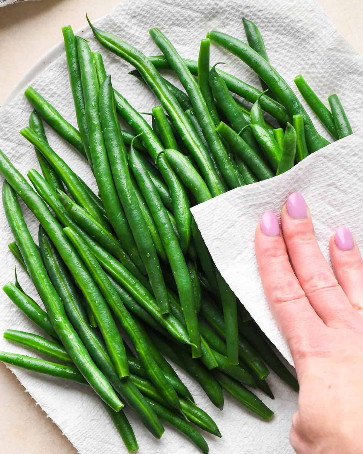 green beans on a paper towel lined plate being patted dry with a paper towel