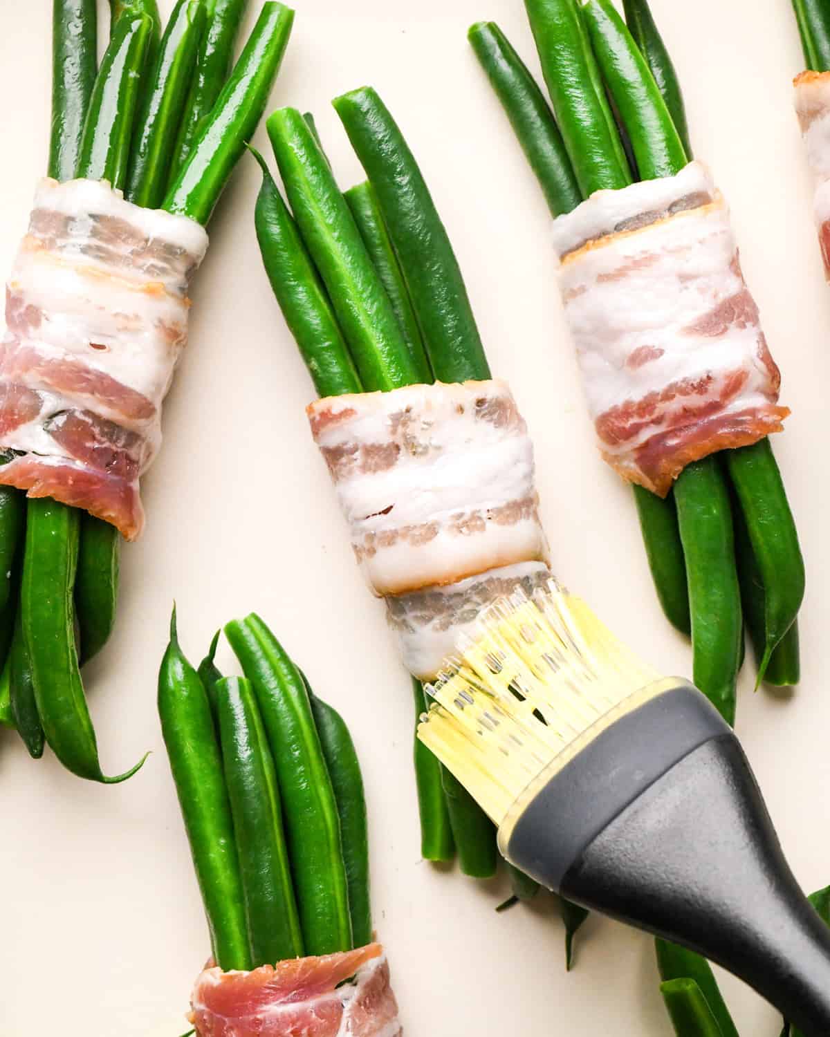 olive oil being spread on a bundle of Bacon Wrapped Green Beans
