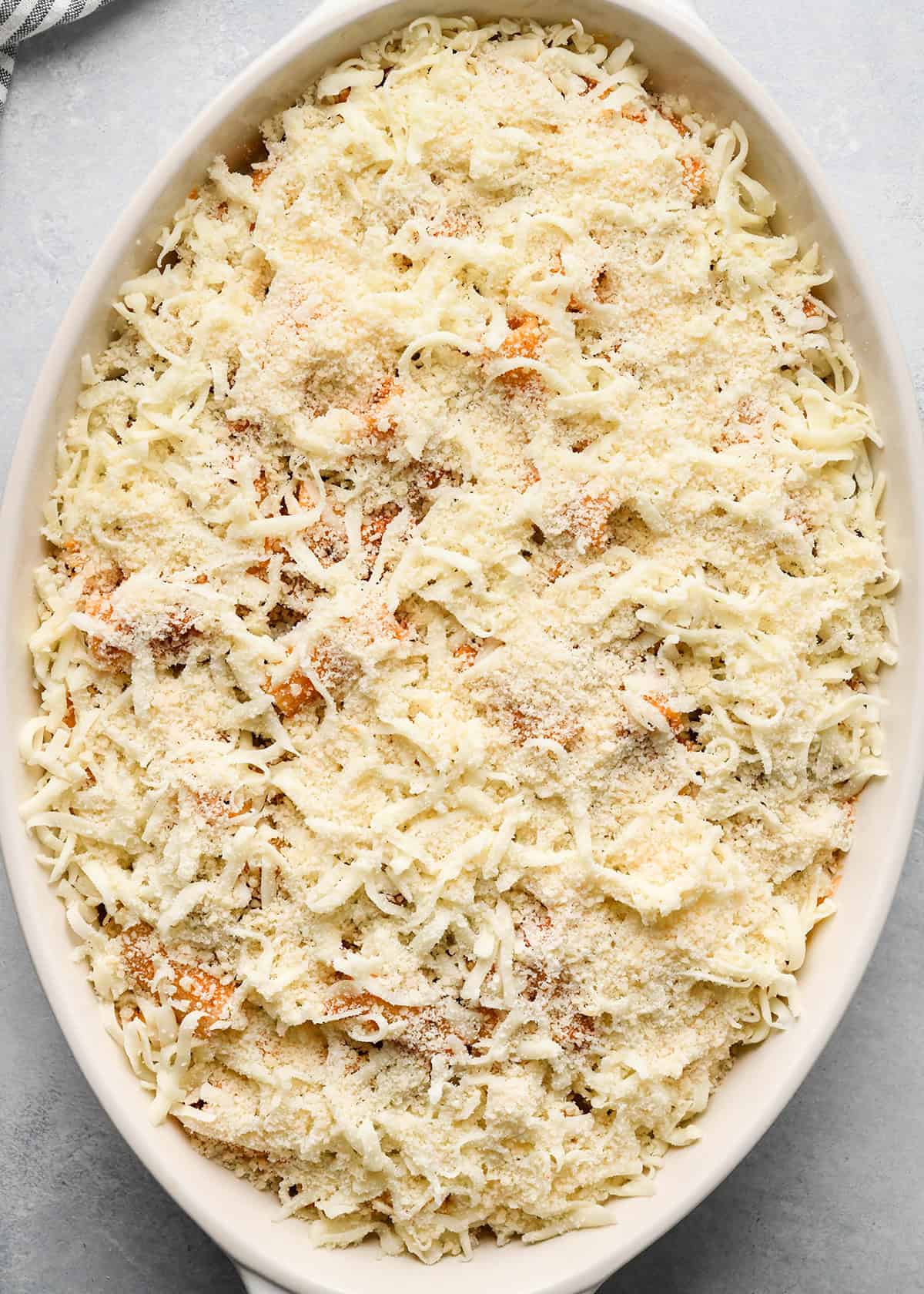 parmesan cheese sprinkled over Baked Mostaccioli mixture in a white baking dish before baking