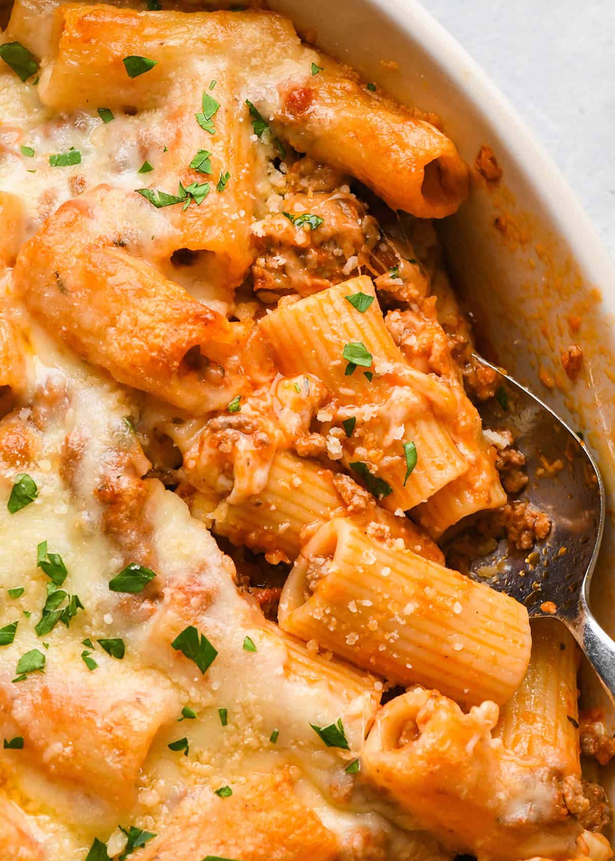close up photo of a spoon taking a scoop of Baked Mostaccioli from a baking dish