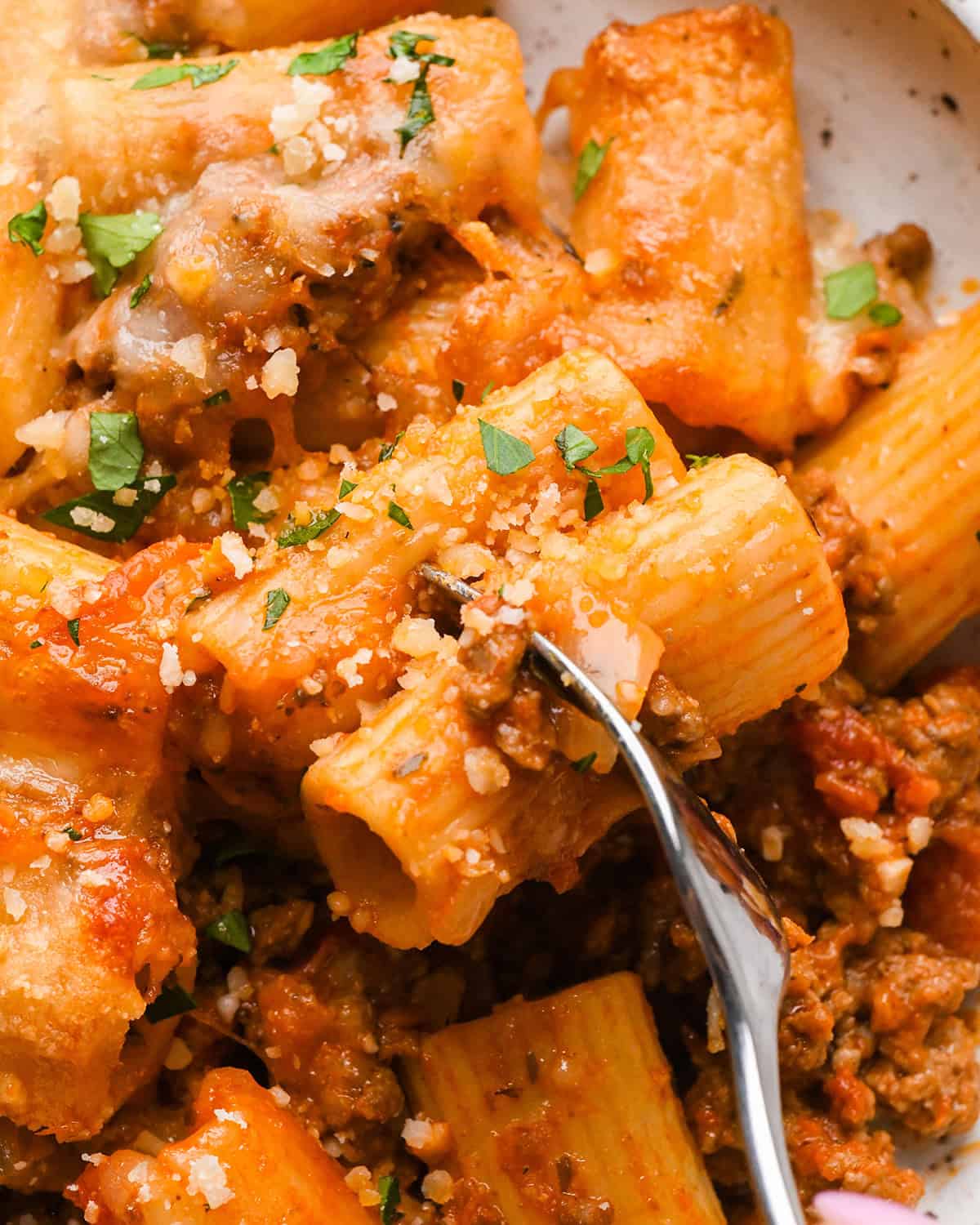 close up photo of a fork taking a bite of Baked Mostaccioli garnished with parsley and parmesan cheese