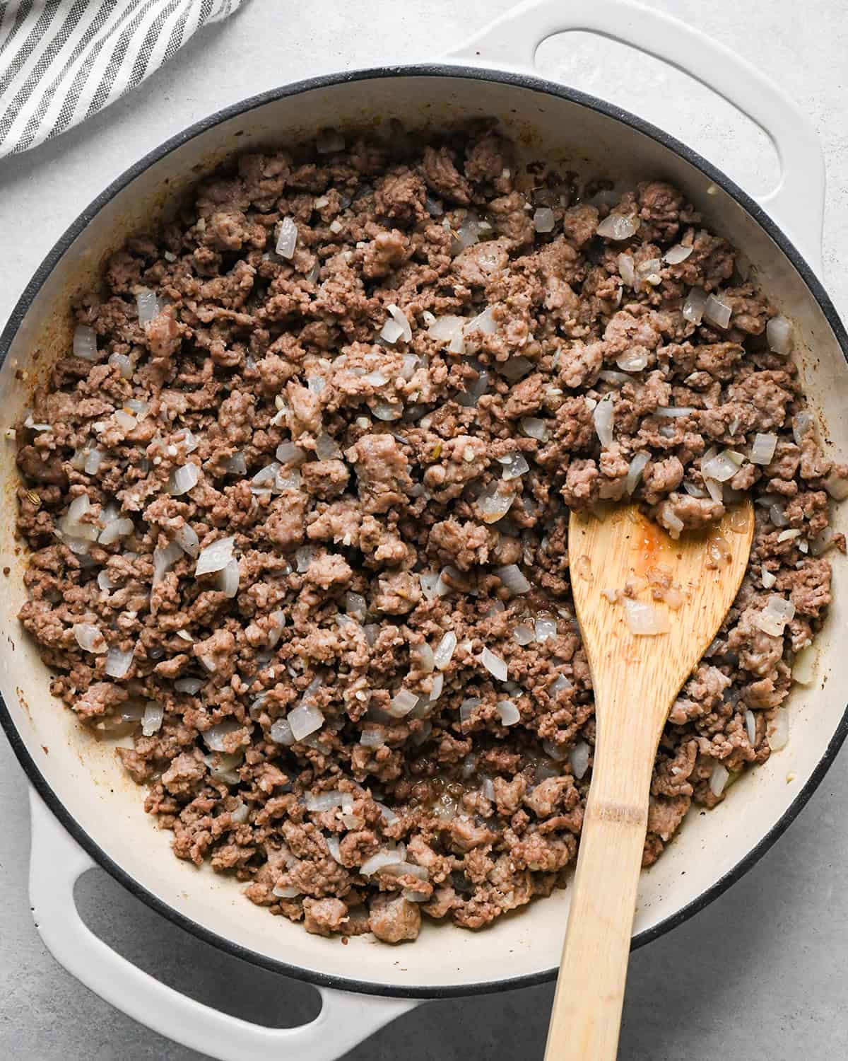 making Baked Mostaccioli - sausage, ground beef, onion and garlic cooked in a skillet with a wooden spatula