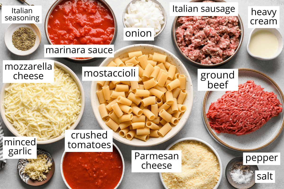 overhead photo of the labeled ingredients in this Baked Mostaccioli recipe like mostaccioli, marinara sauce, ground beef, sausage, mozzarella, parmesan and mroe