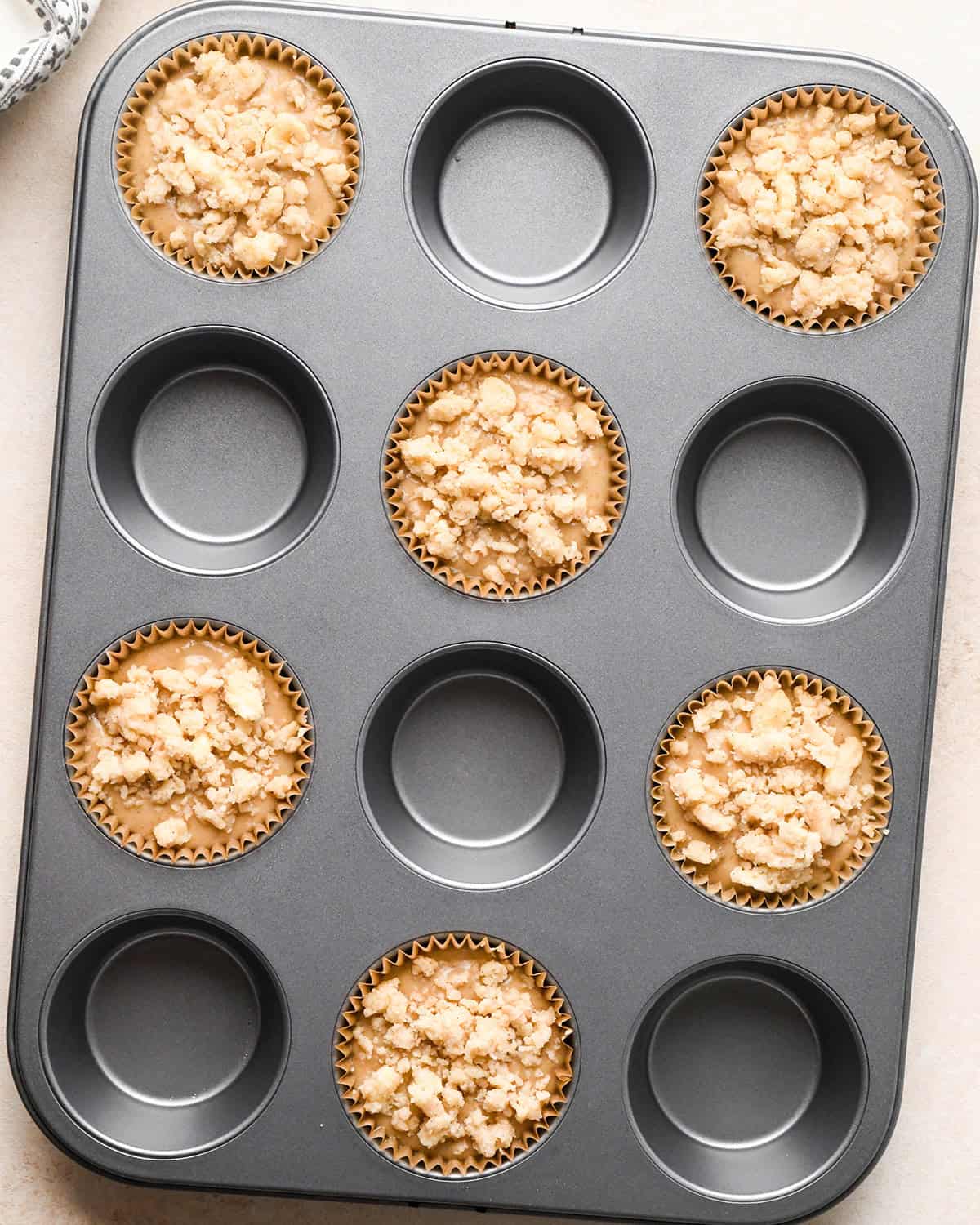 6 banana crumb muffins with topping in a muffin pan before baking