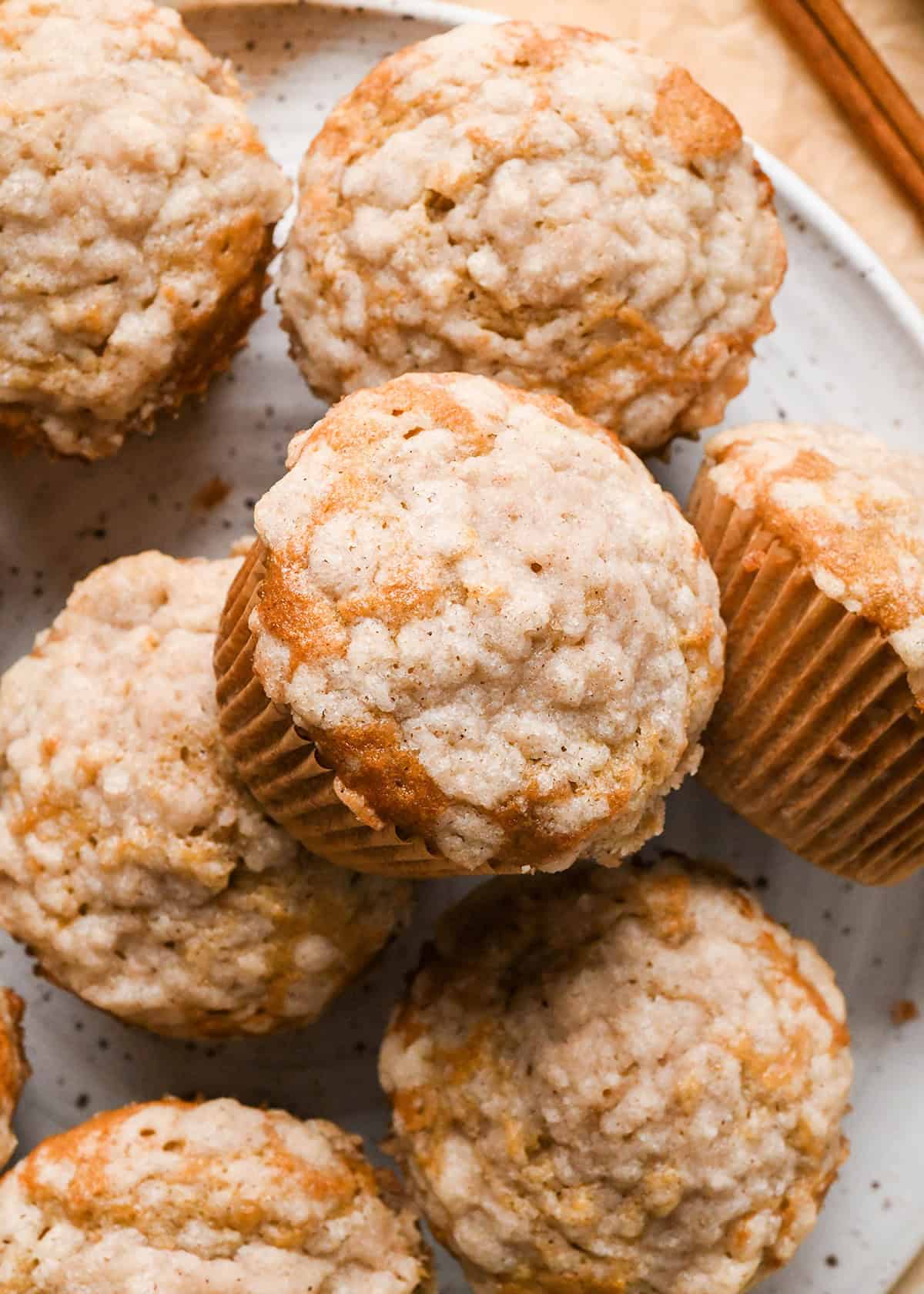 7 banana crumb muffins with a streusel topping, stacked on a white plate