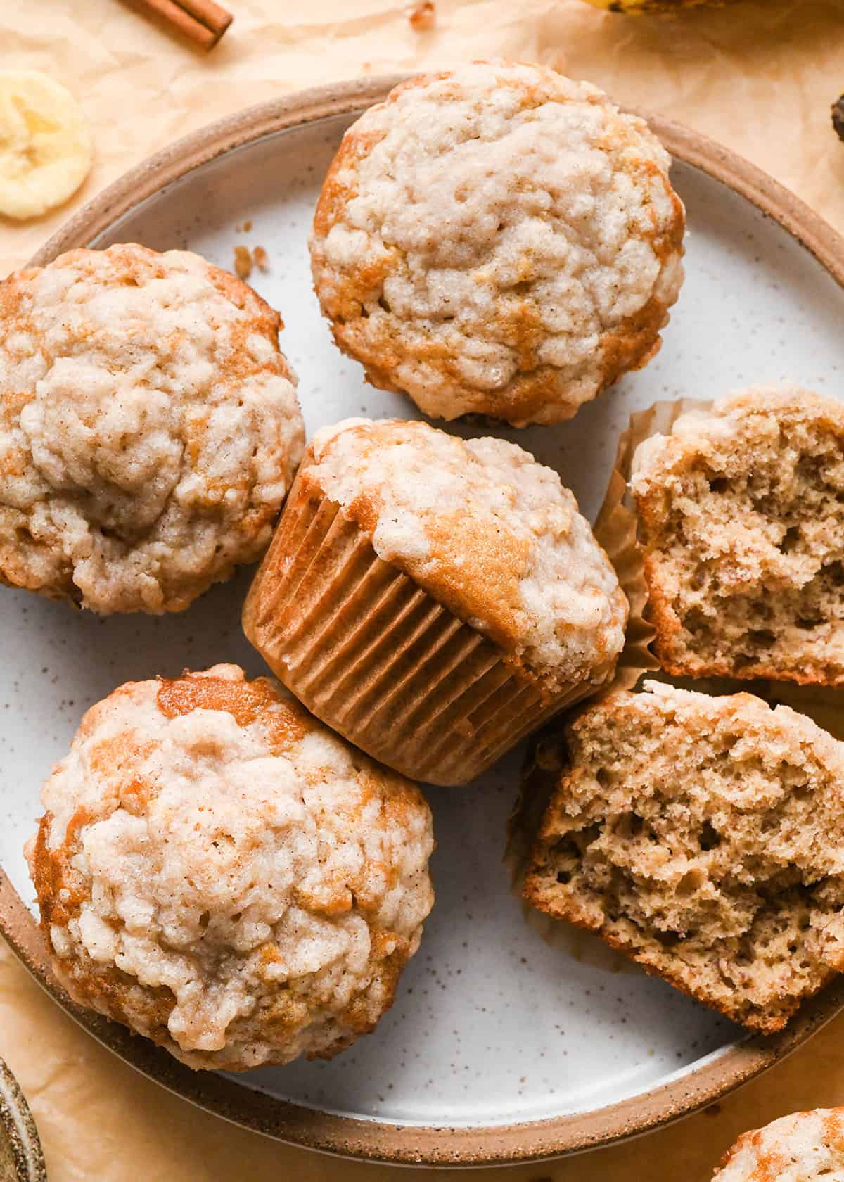 5 banana crumb muffins with streusel topping on a plate, one cut in half so the inside is visible.