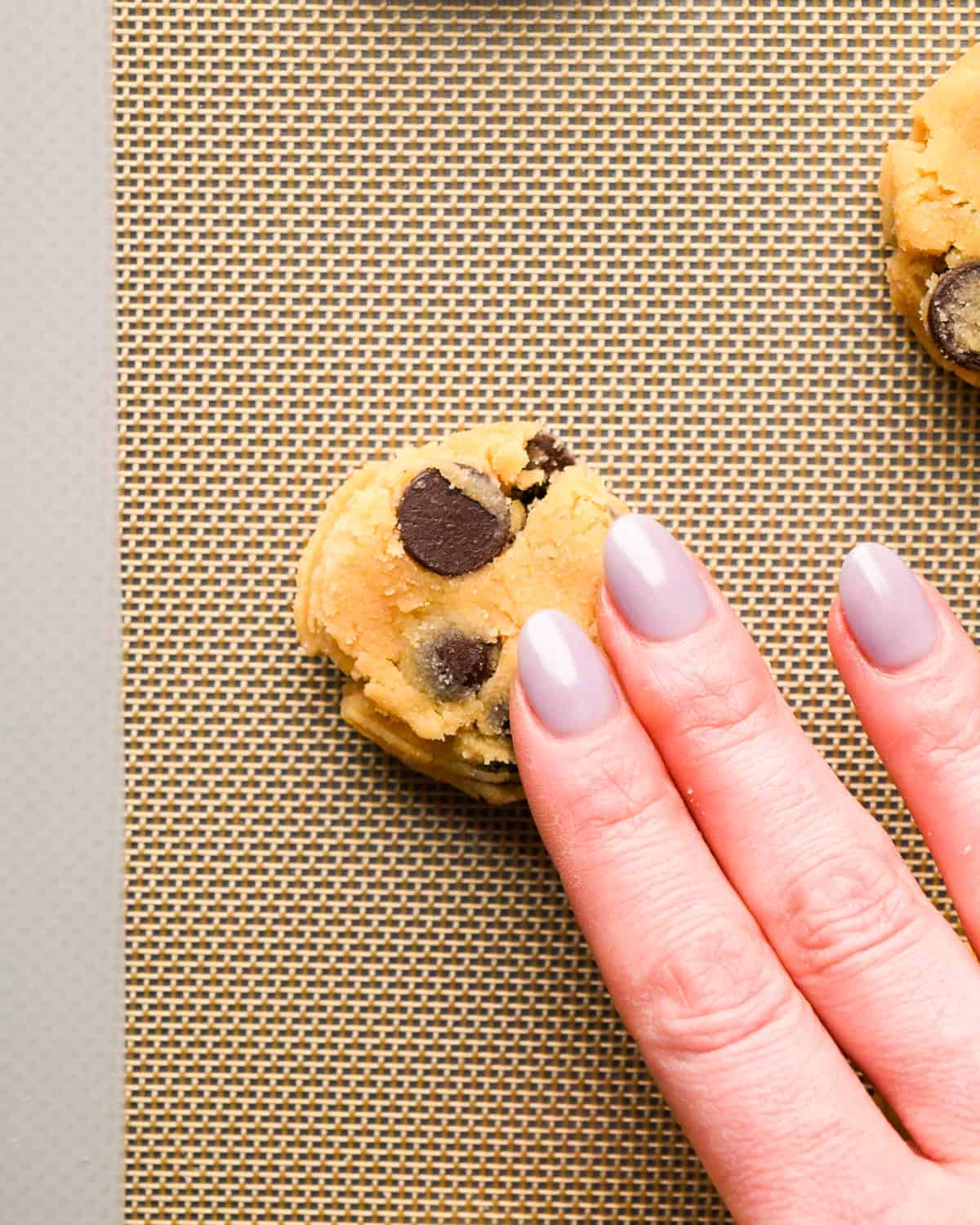 a hand pressing down a Coconut Flour Cookie dough ball on a baking sheet