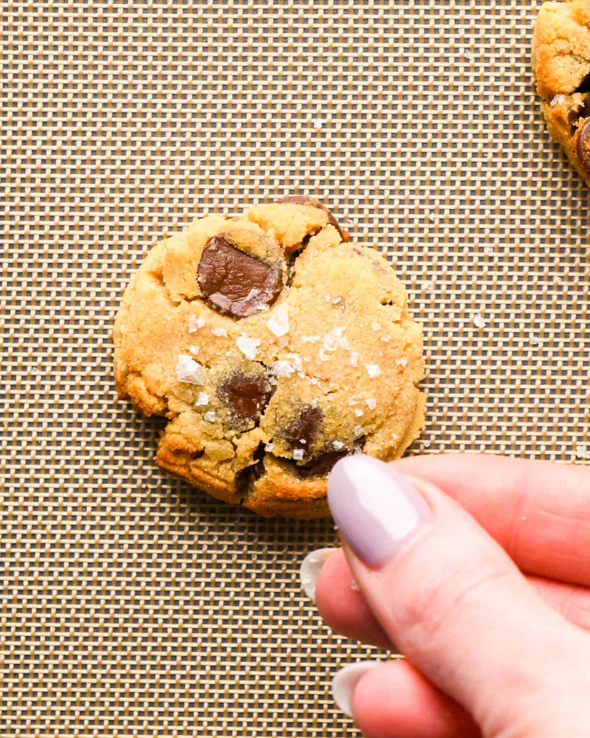 a hand sprinkling sea salt on Coconut Flour Cookies