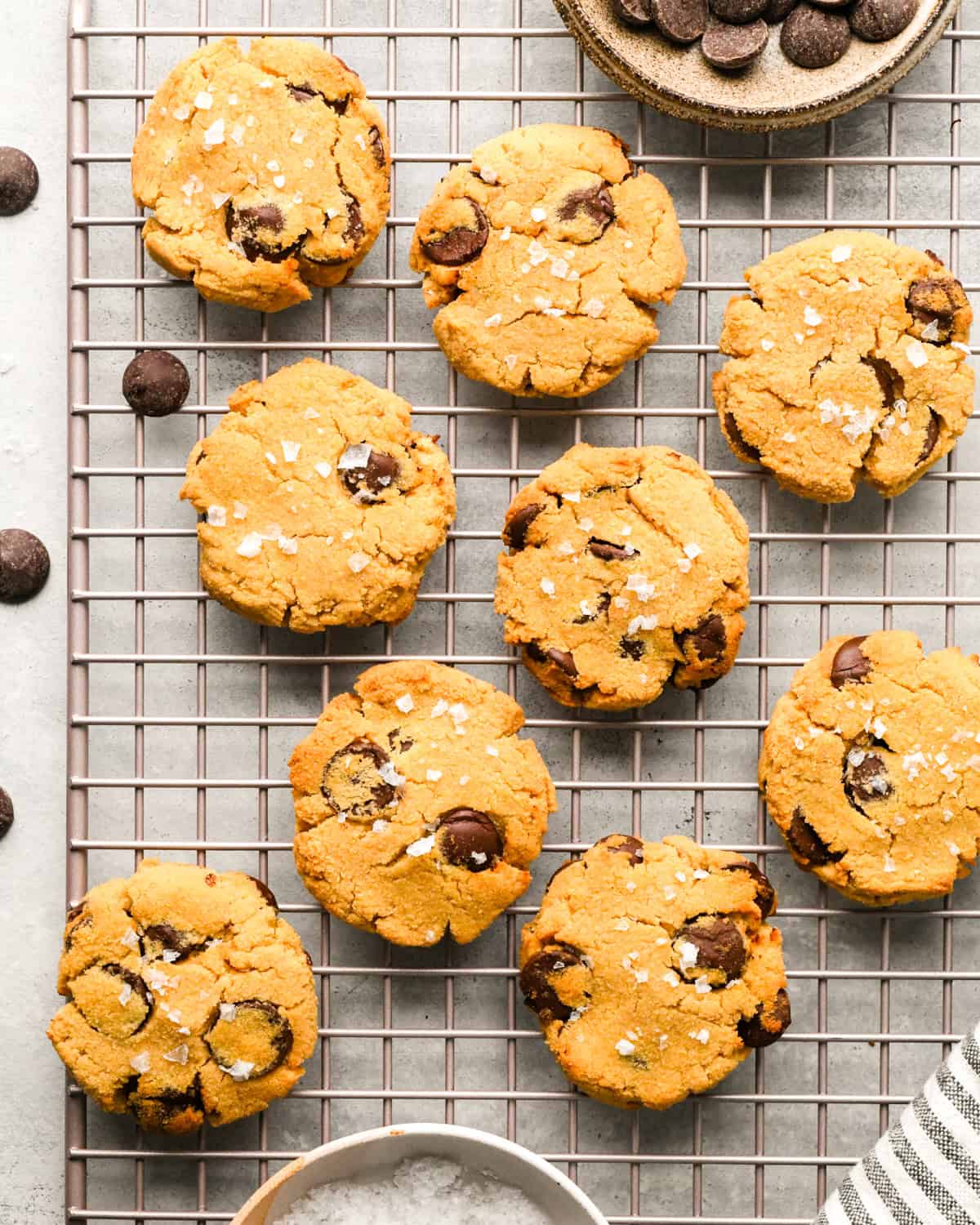 9 Coconut Flour Cookies topped with flaky sea salt on a wire cooling rack on a gray surface 