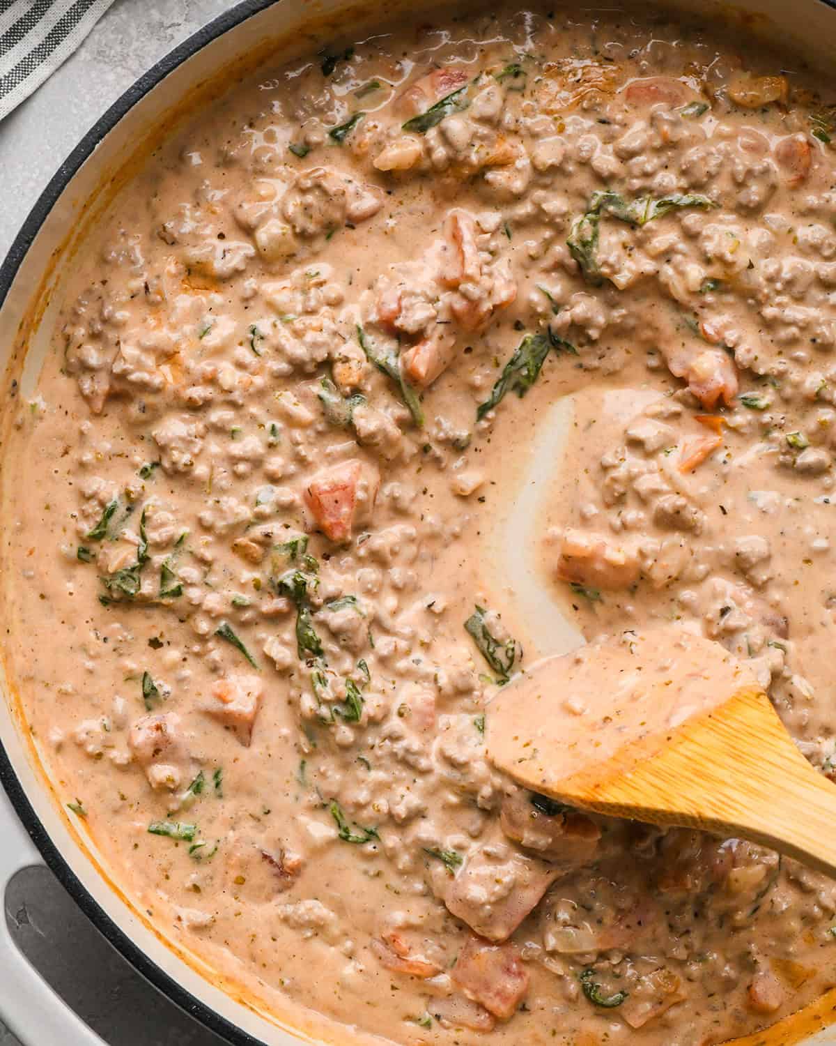 up close photo of a wooden spatula stirring Ground Beef Tortellini sauce in a pan