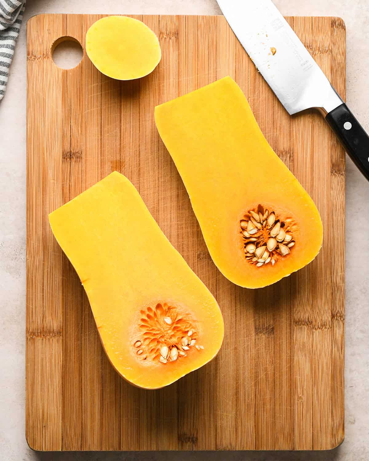 Halved butternut squash with seeds on a wooden cutting board next to a knife to be used to make butternut squash risotto