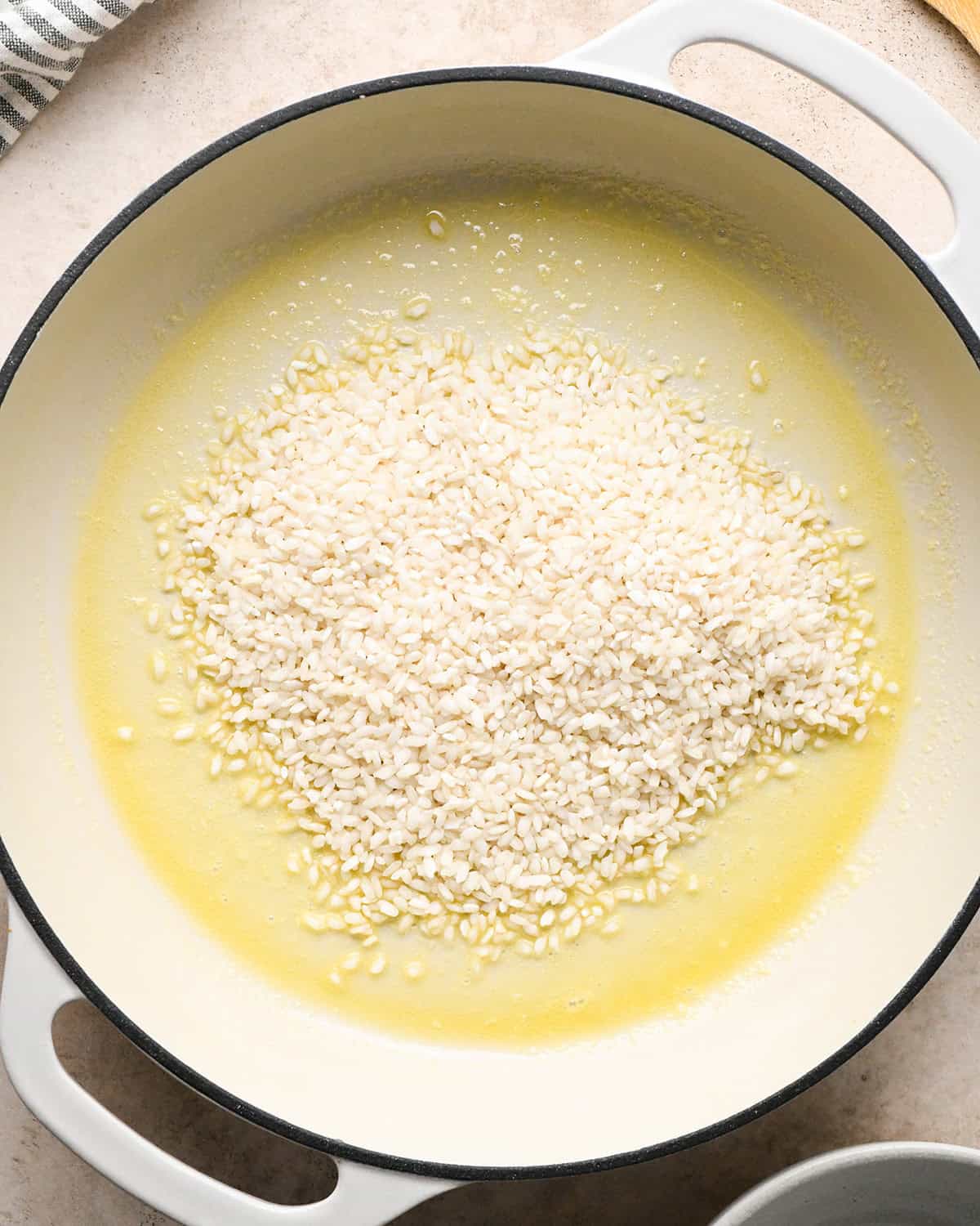 Making butternut squash risotto - butter and rice in a white 5-quart saucepan