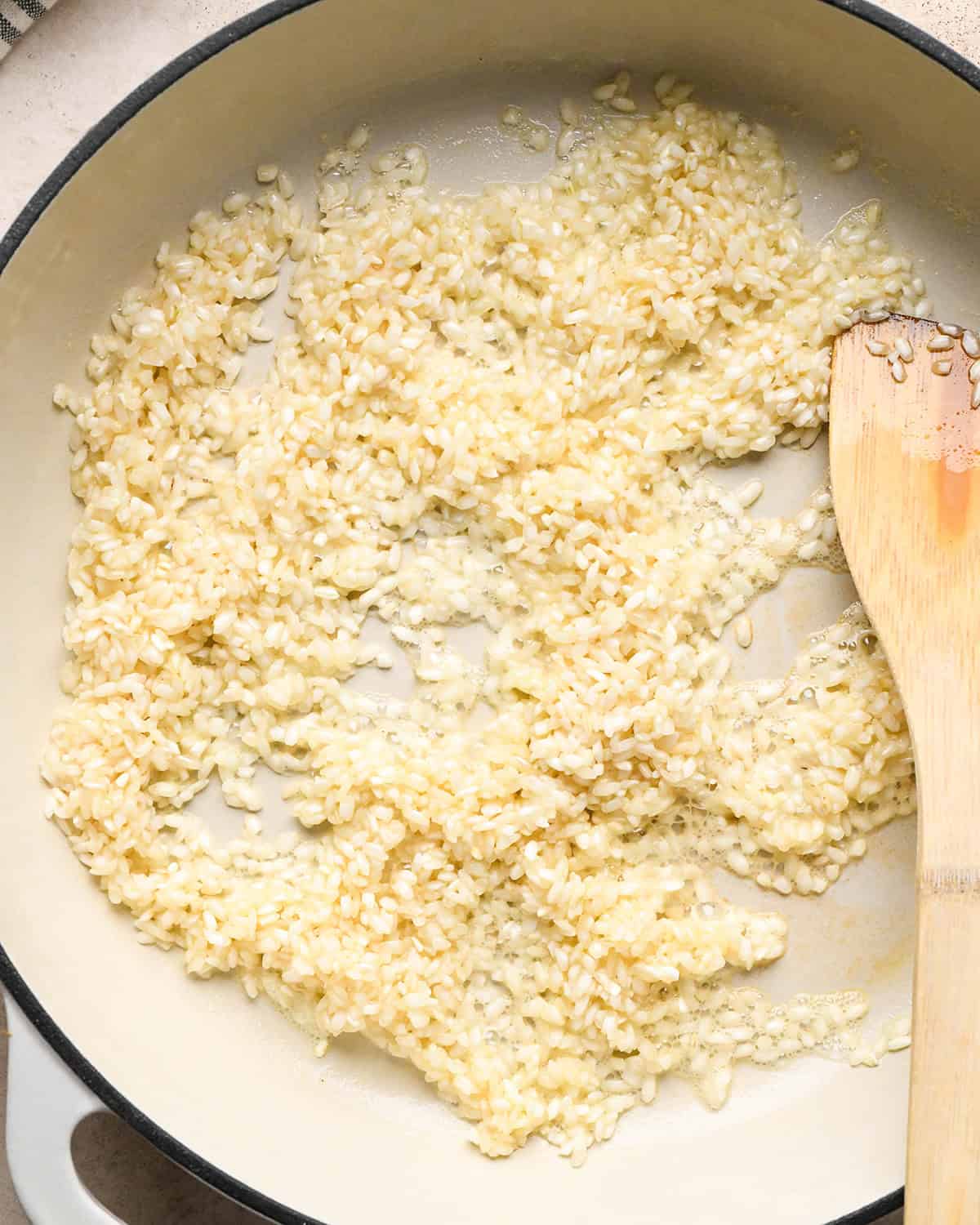 Making butternut squash risotto - butter and rice in a white 5-quart saucepan being stirred with a wooden spoon