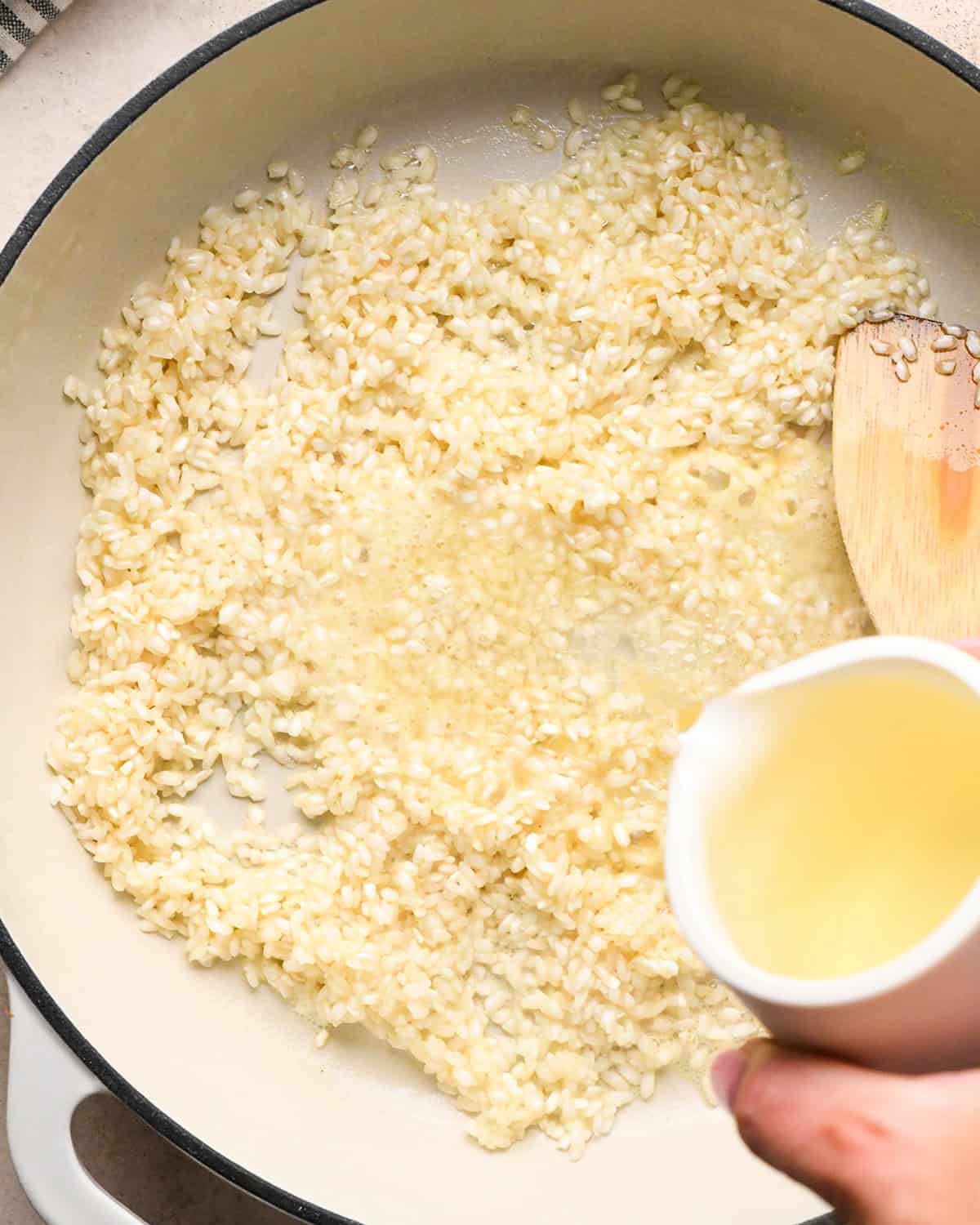 Making butternut squash risotto - pouring white wine into a white 5-quart saucepan with butter and rice, stirred with a wooden spoon