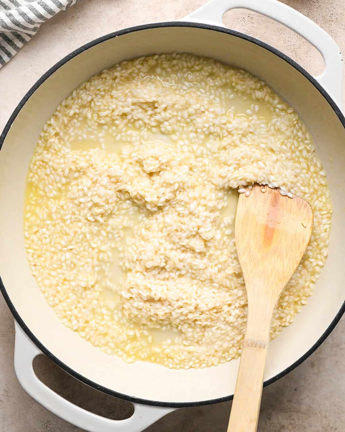 Making butternut squash risotto - pouring butternut squash mixture into a white 5-quart saucepan with butter, rice, and white wine