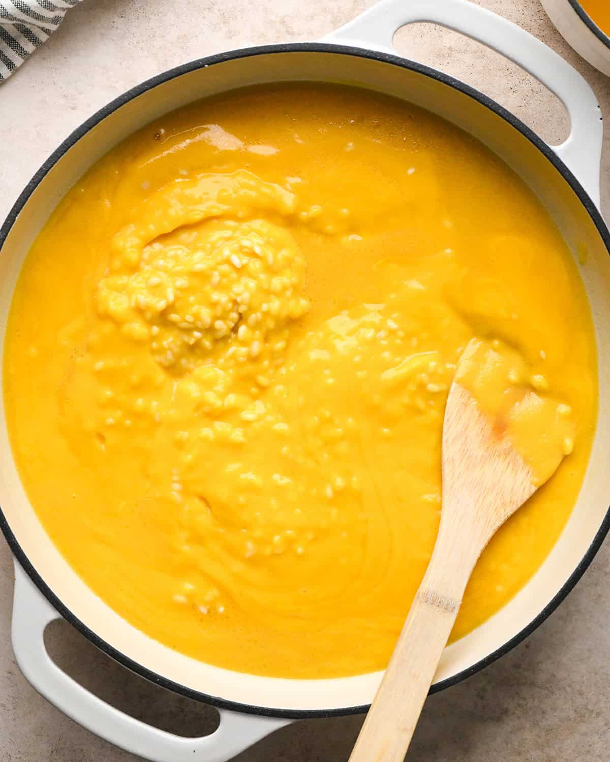 Making butternut squash risotto - all ingredients in a white saucepan being stirred with a wooden spoon