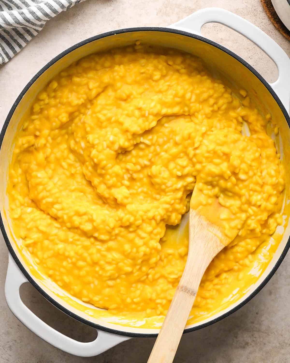 Making butternut squash risotto - all ingredients in a white saucepan being stirred with a wooden spoon