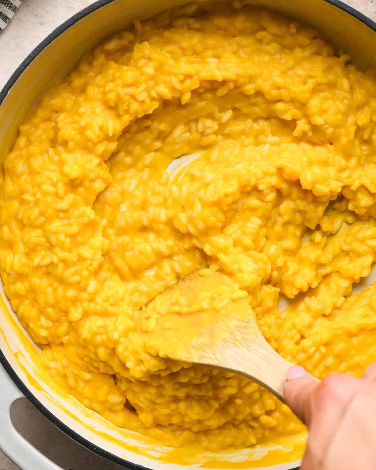 Making butternut squash risotto - all ingredients in a white saucepan, being stirred with a wooden spoon