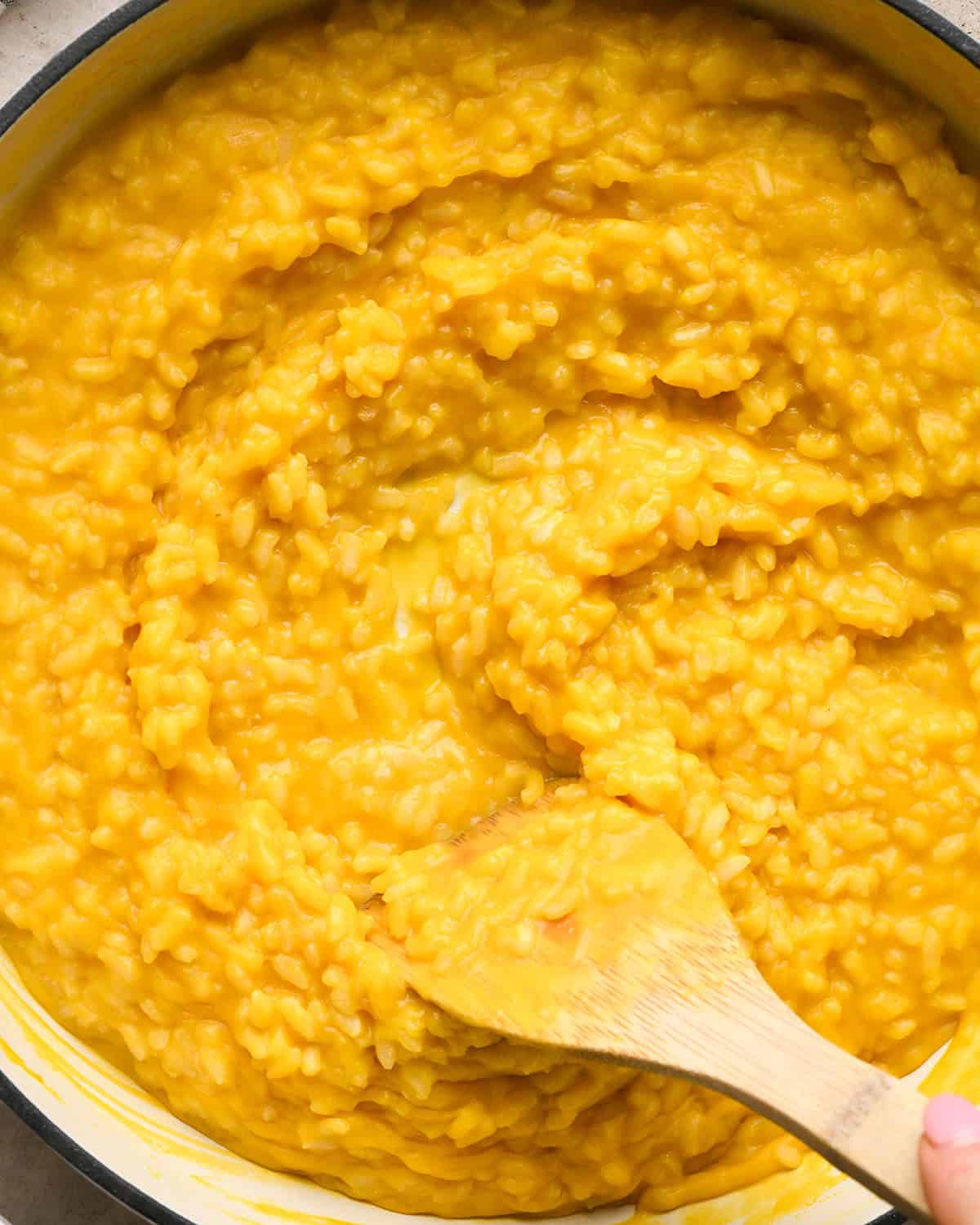 Making butternut squash risotto - all ingredients in a white saucepan, being stirred with a wooden spoon