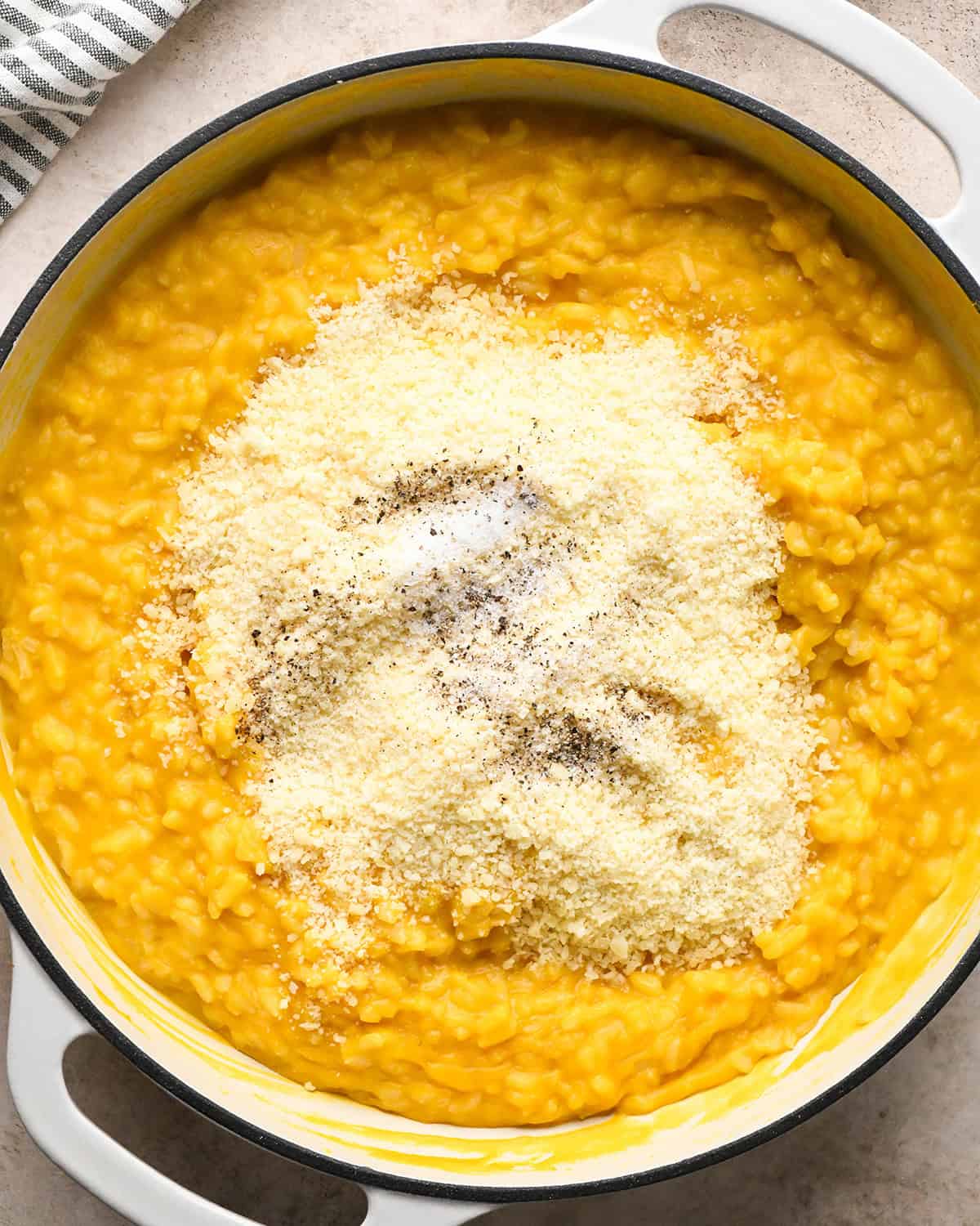 Making butternut squash risotto - adding sea salt, pepper, and parmesan cheese to butternut squash risotto in a white saucepan