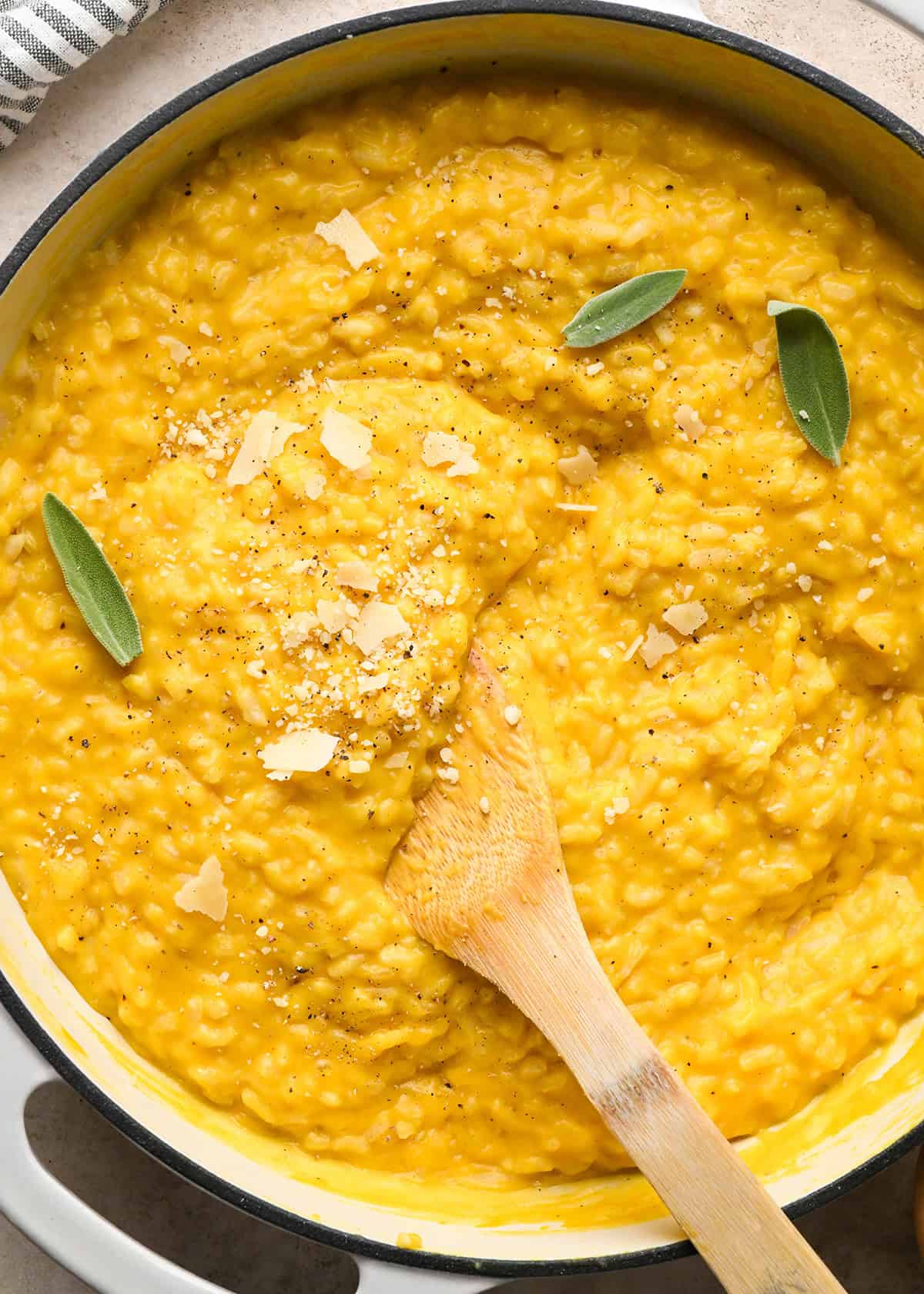 Making butternut squash risotto - adding sage to butternut squash risotto in a white saucepan and serving with a wooden spoon