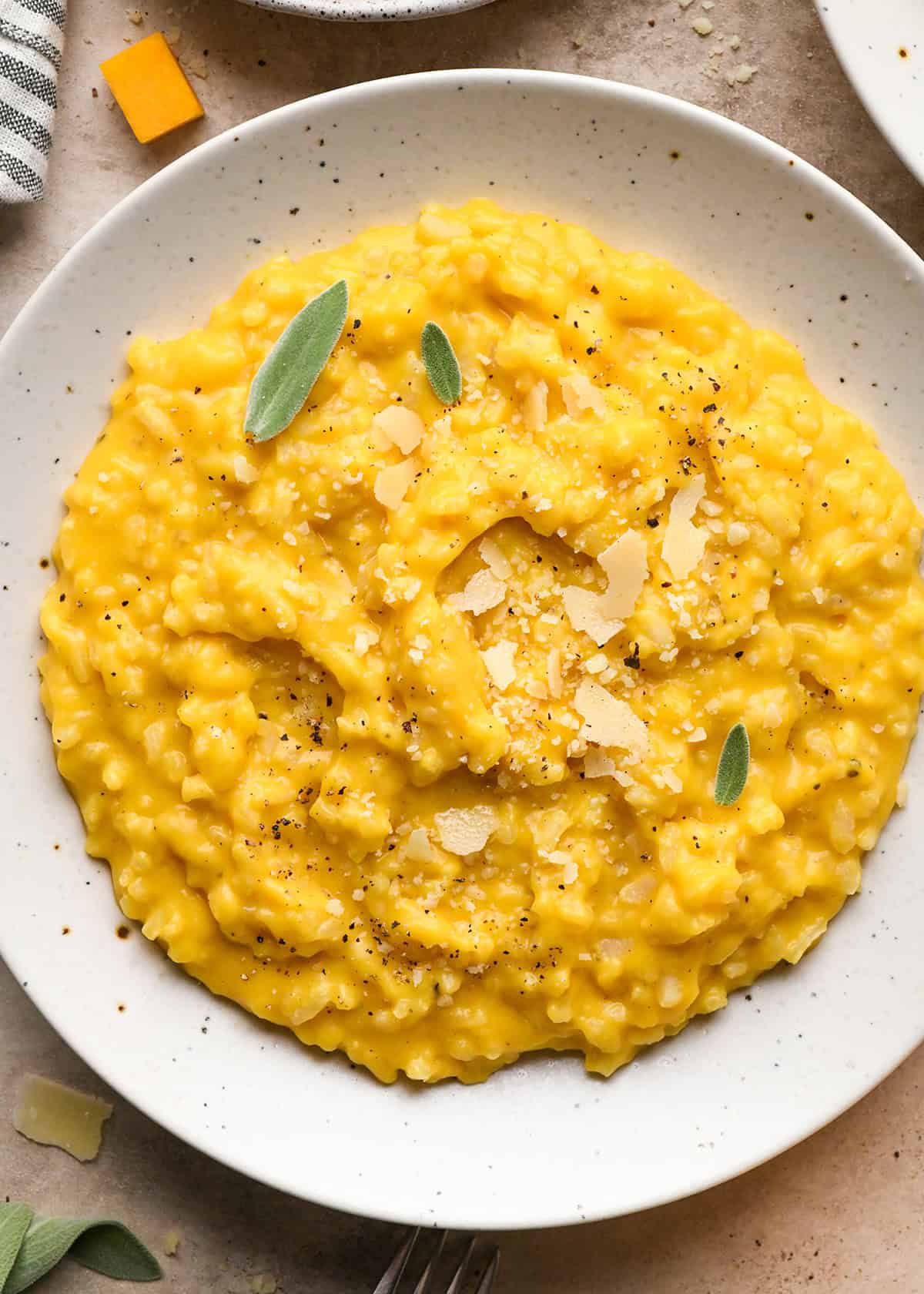 overhead photo of butternut squash risotto served on a white speckled plate and topped with sage, parmesan cheese, and pepper