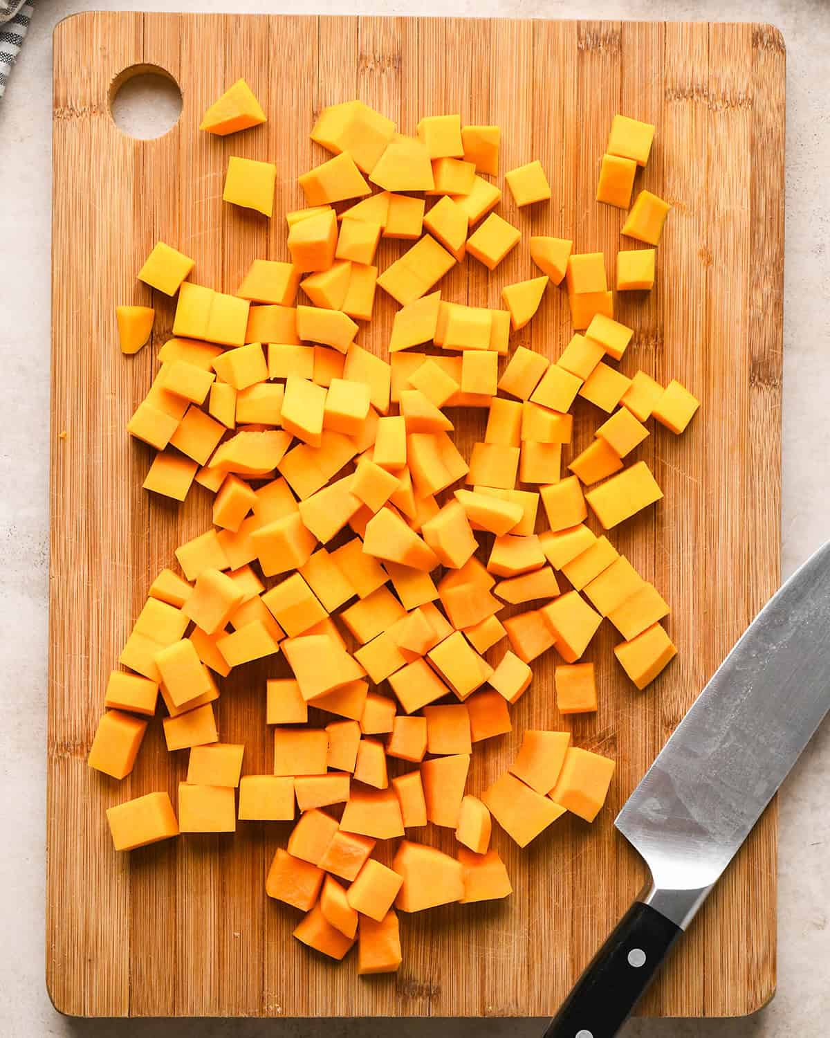 Overhead photo of diced butternut squash on a wooden cutting board next to a knife