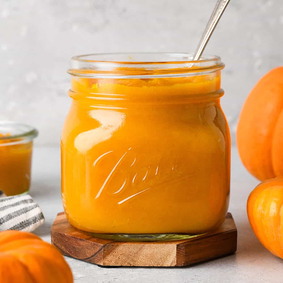 front view of a glass jar filled with pumpkin puree and a spoon