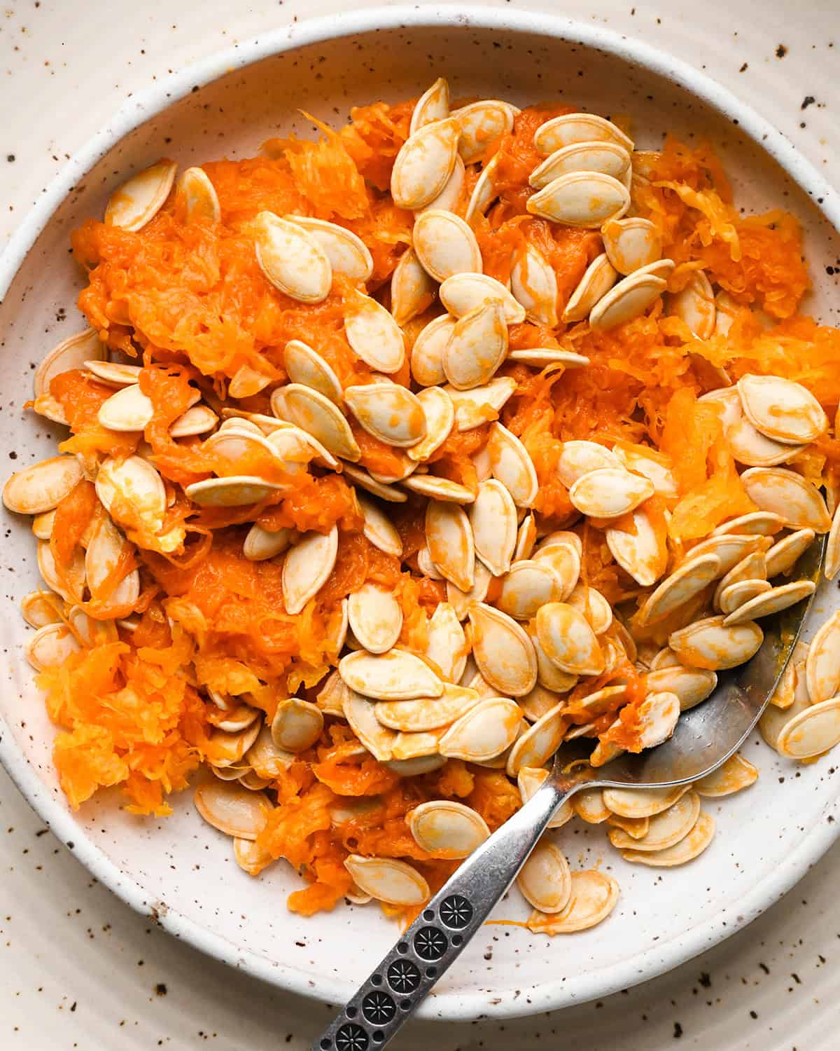 fibrous strands and seeds from a pumpkin in a bowl with a spoon