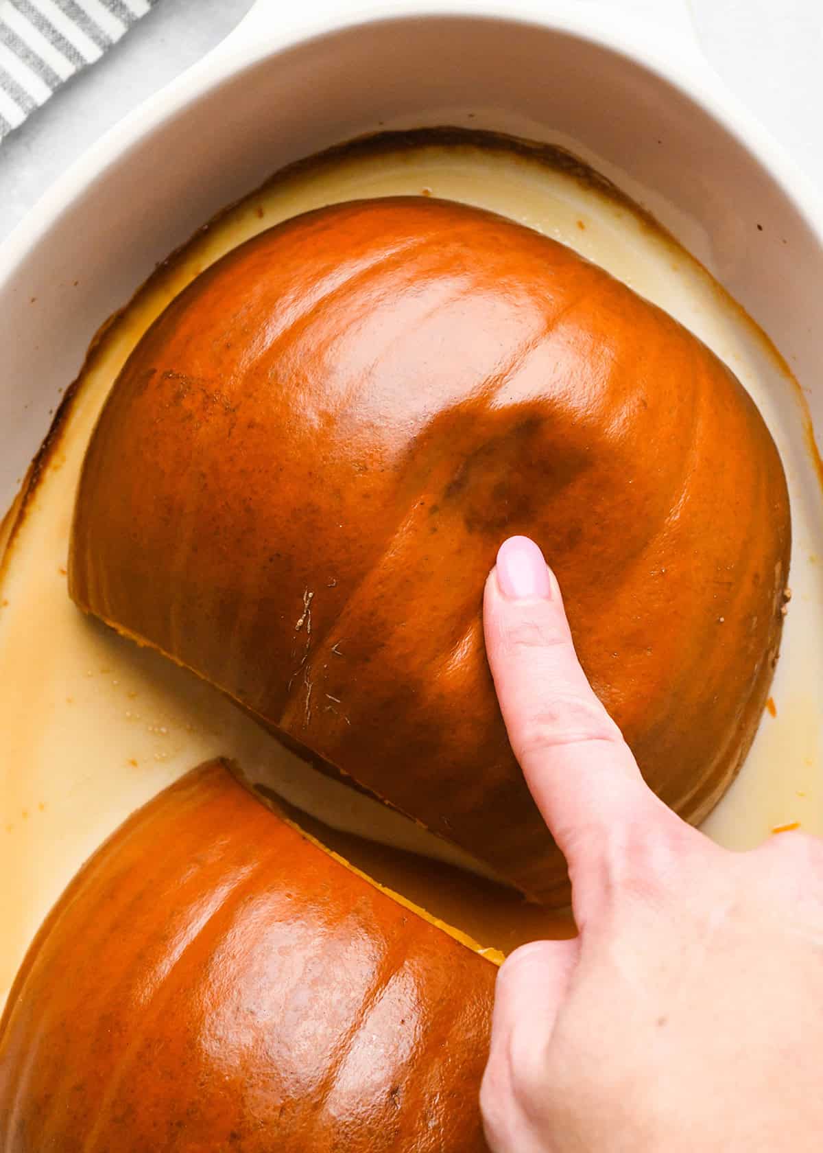 How to Make Pumpkin Puree - a hand pressing an indent into a baked pumpkin