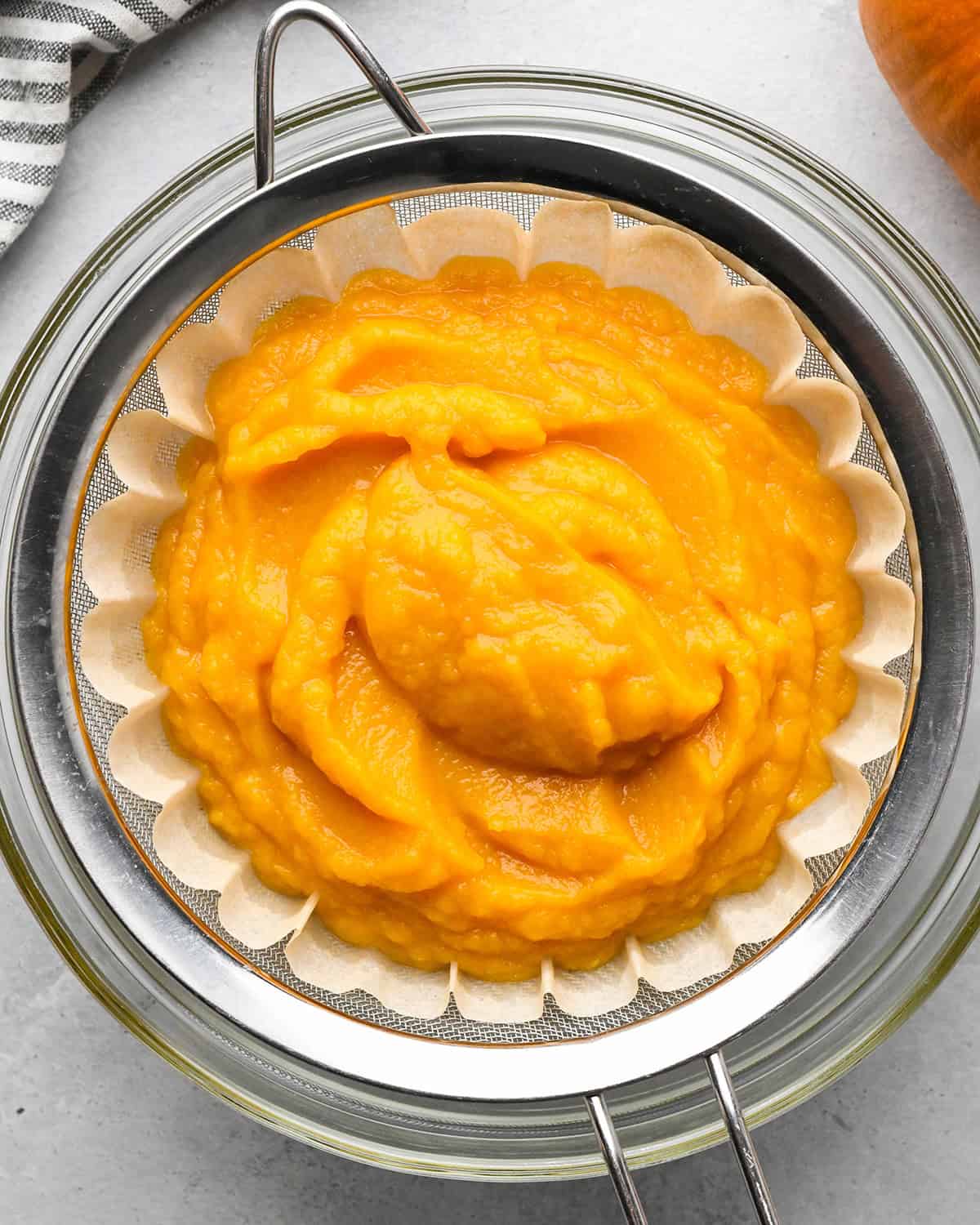 How to Make Pumpkin Puree - pumpkin puree in a coffee filter in a fine mesh metal strainer over a bowl