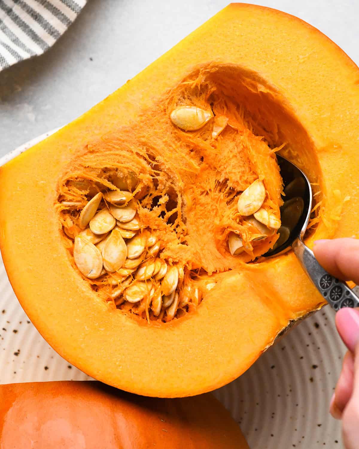 How to Make Pumpkin Puree - a spoon scooping the inside fibrous strands and seeds out of one half of a pie pumpkin