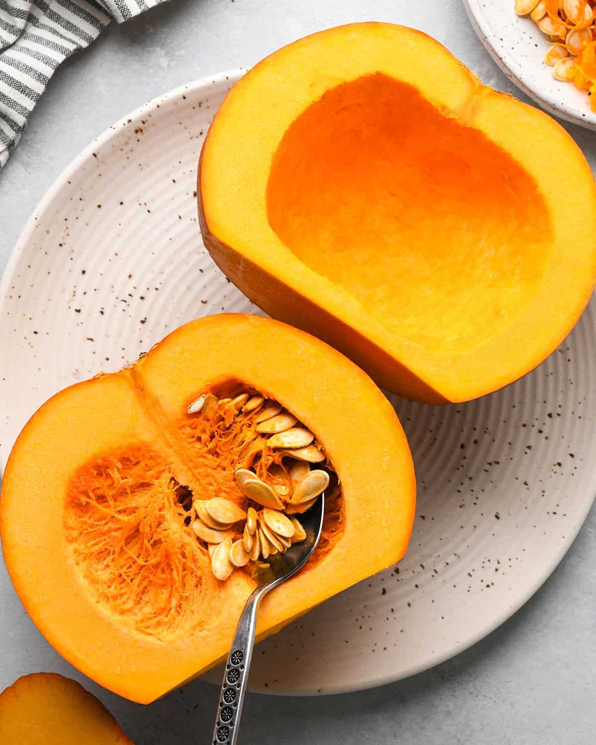 How to Make Pumpkin Puree - two halves of a pumpkin on a plate, one with seeds removed, one with a spoon in the seeds 