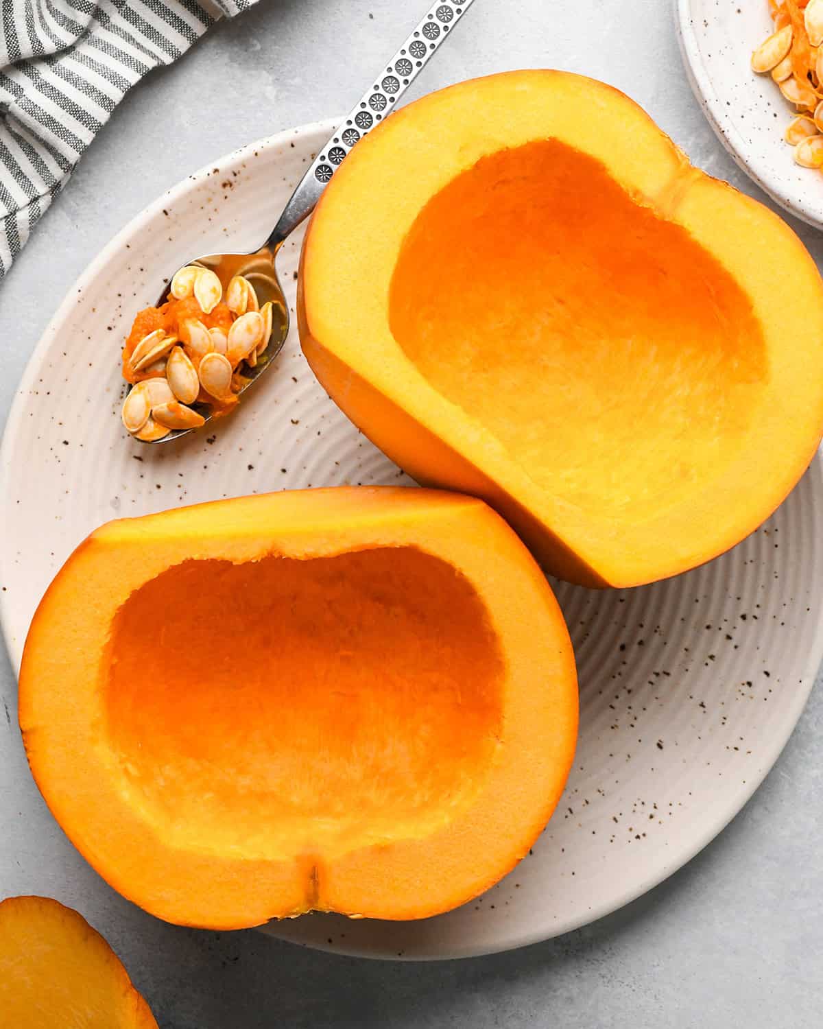 two halves of a pumpkin on a plate with the fibrous strands and seeds removed, face up. 