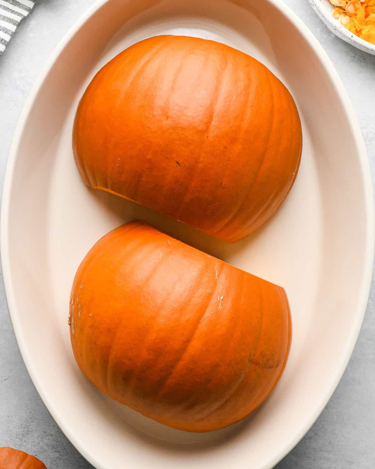 How to Make Pumpkin Puree - two halves of a pumpkin, inside down, in a white oval baking dish before baking