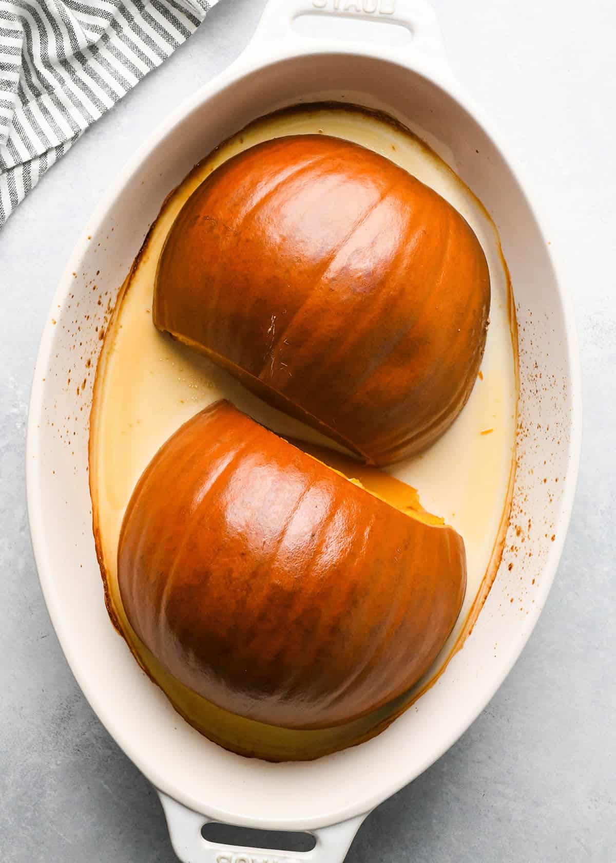 How to Make Pumpkin Puree - two halves of a pumpkin, inside down, in a white oval baking dish after baking