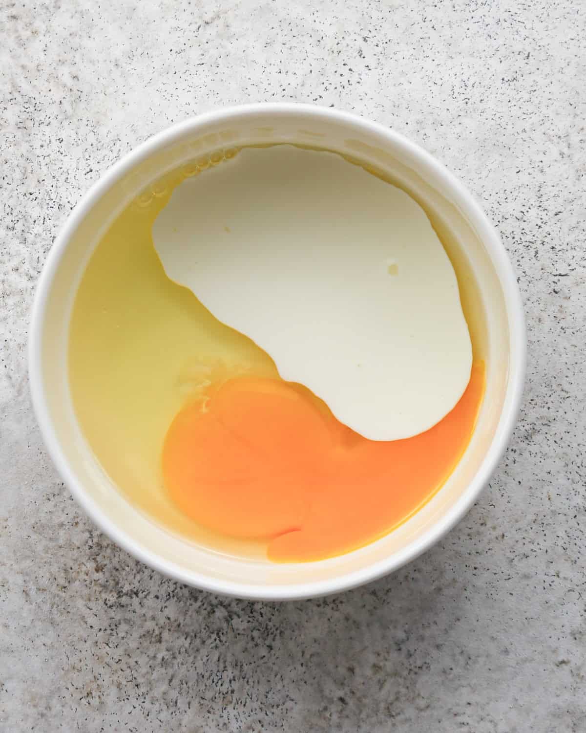 egg and heavy cream in a small white bowl on a gray surface before mixing making the egg wash for pie crust cookies