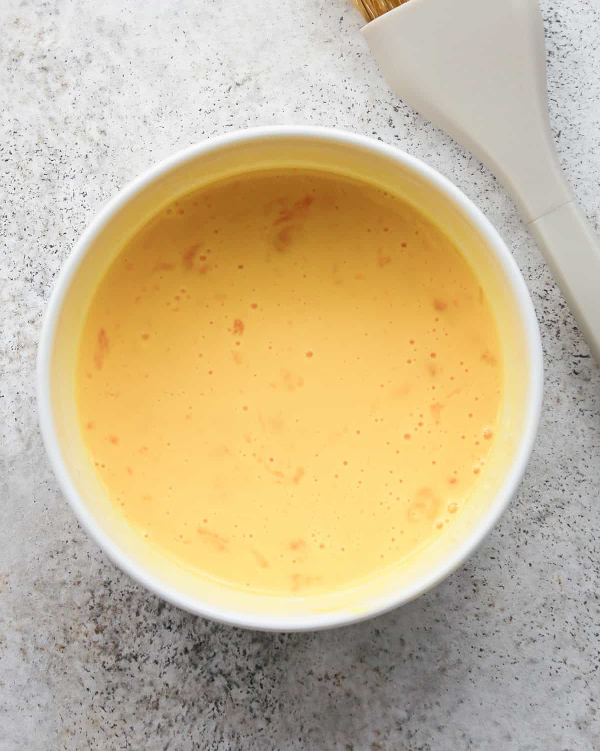 egg wash for pie crust cookies in a small white bowl on a gray surface with a gray pastry brush next to it