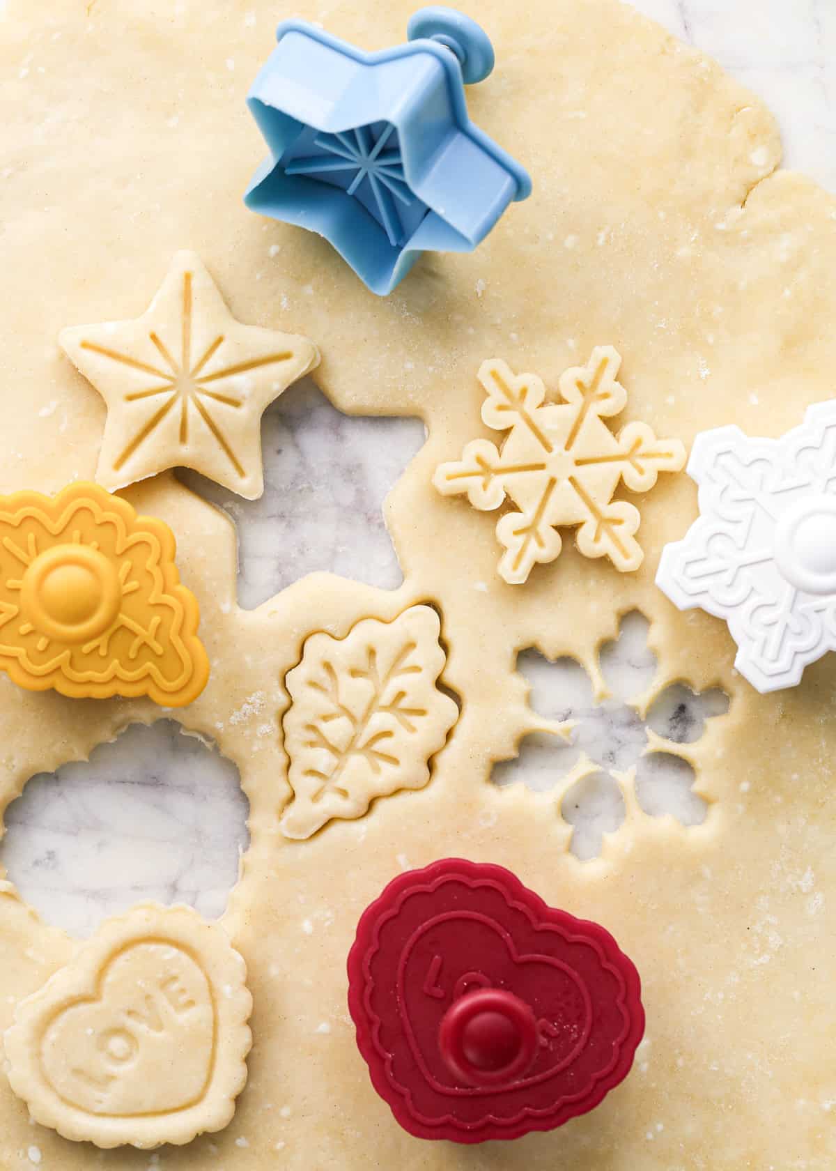 close up of 4 pie curst cutters in the shape of a star, leaf, snowflake and heart cutting shapes out of pie dough to make pie crust cookies