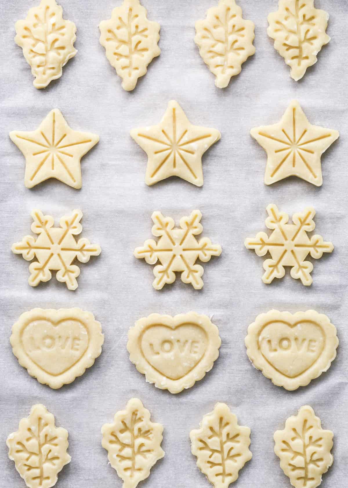 5 rows of pie crust cookies cut into leaves, stars, snowflakes and hearts on a baking sheet lined with parchment paper before baking