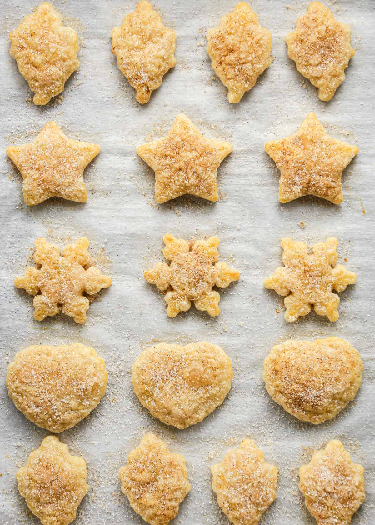 17 Pie Crust Cookies with cinnamon sugar in the shapes of hearts, stars, leaves and snowflakes arranged in 5 rows on a parchment-lined baking sheet after baking