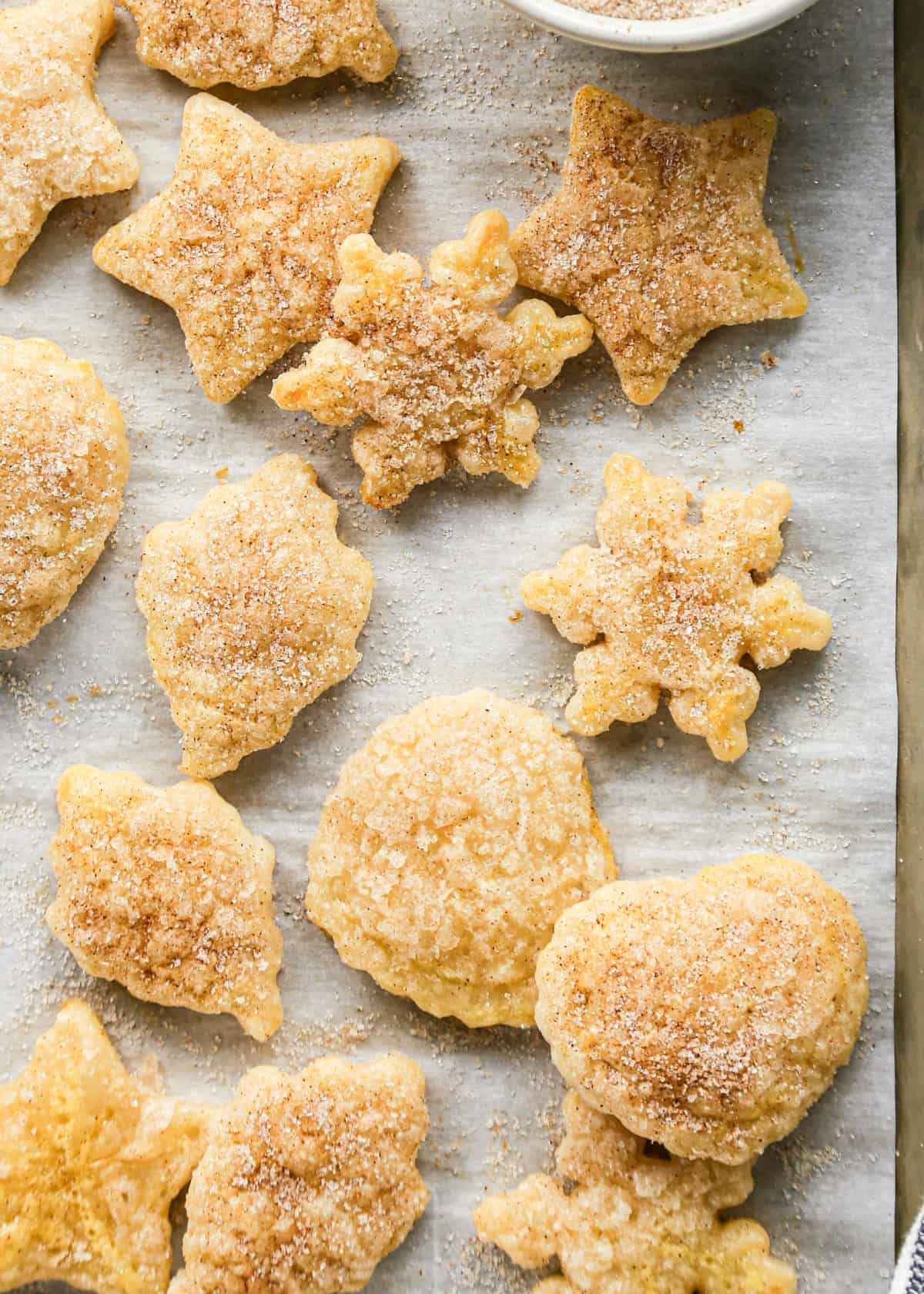 12 Pie Crust Cookies with cinnamon sugar in the shapes of hearts, stars, leaves and snowflakes on parchment paper on a baking sheet