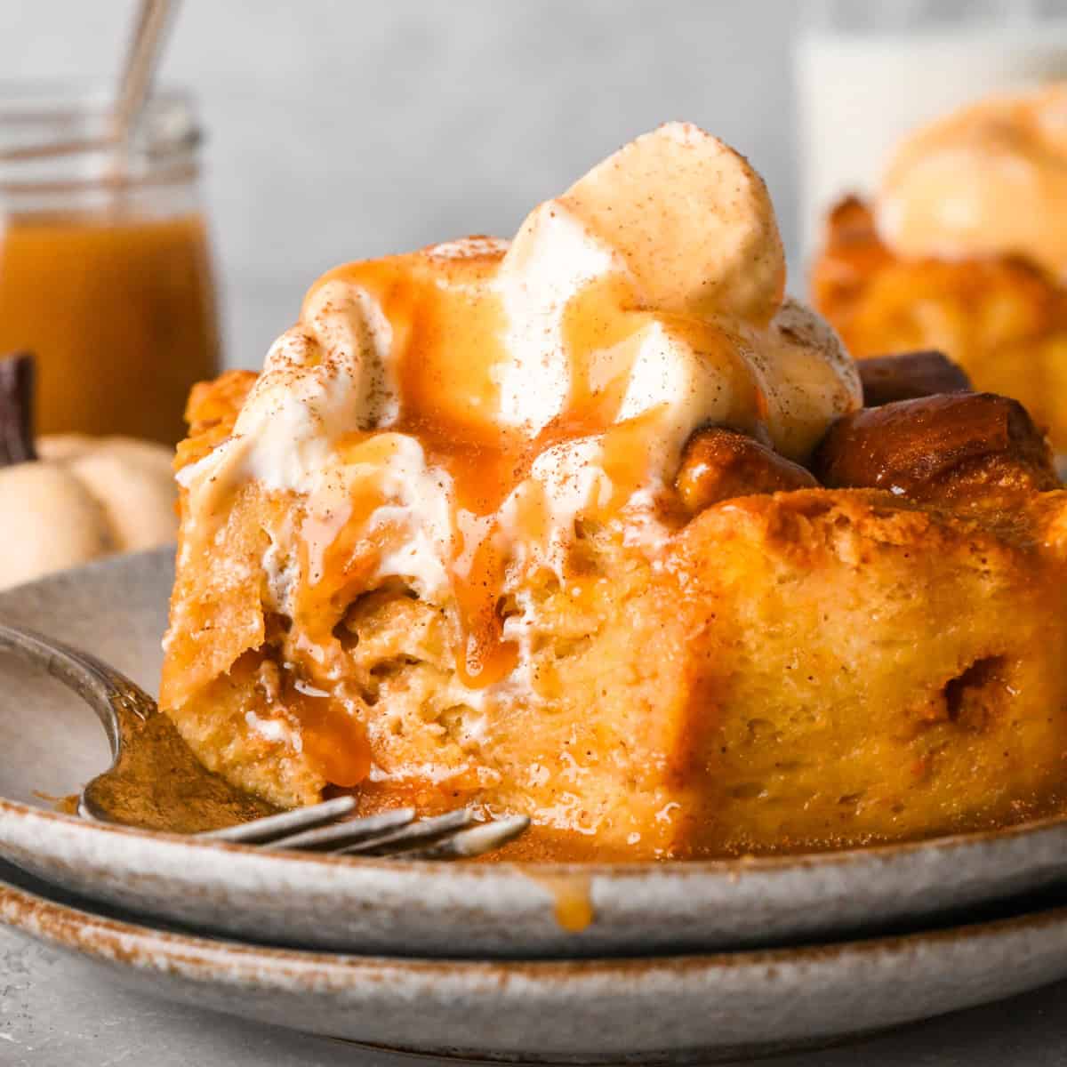 Pumpkin Bread Pudding on a plate with a fork and a bite taken out of it topped with ice cream, caramel sauce and cinnamon. 