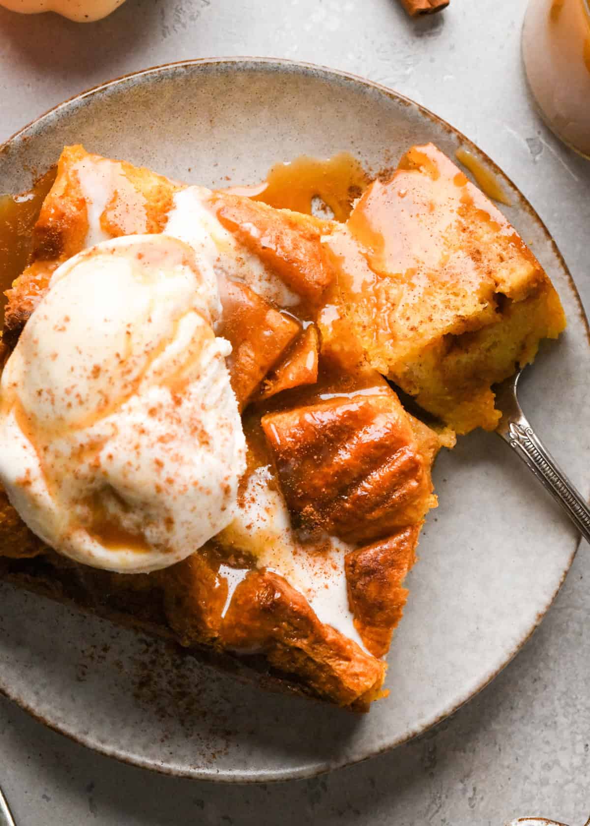 Pumpkin Bread Pudding on a plate with a bite on a fork, topped with ice cream, cinnamon and caramel sauce