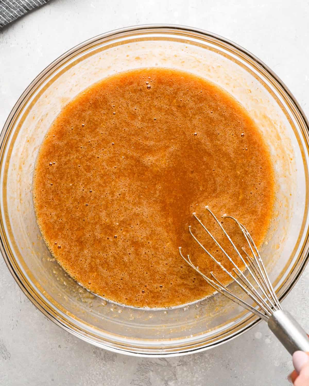 pumpkin custard mixture in a glass bowl with a whisk on a gray surface 